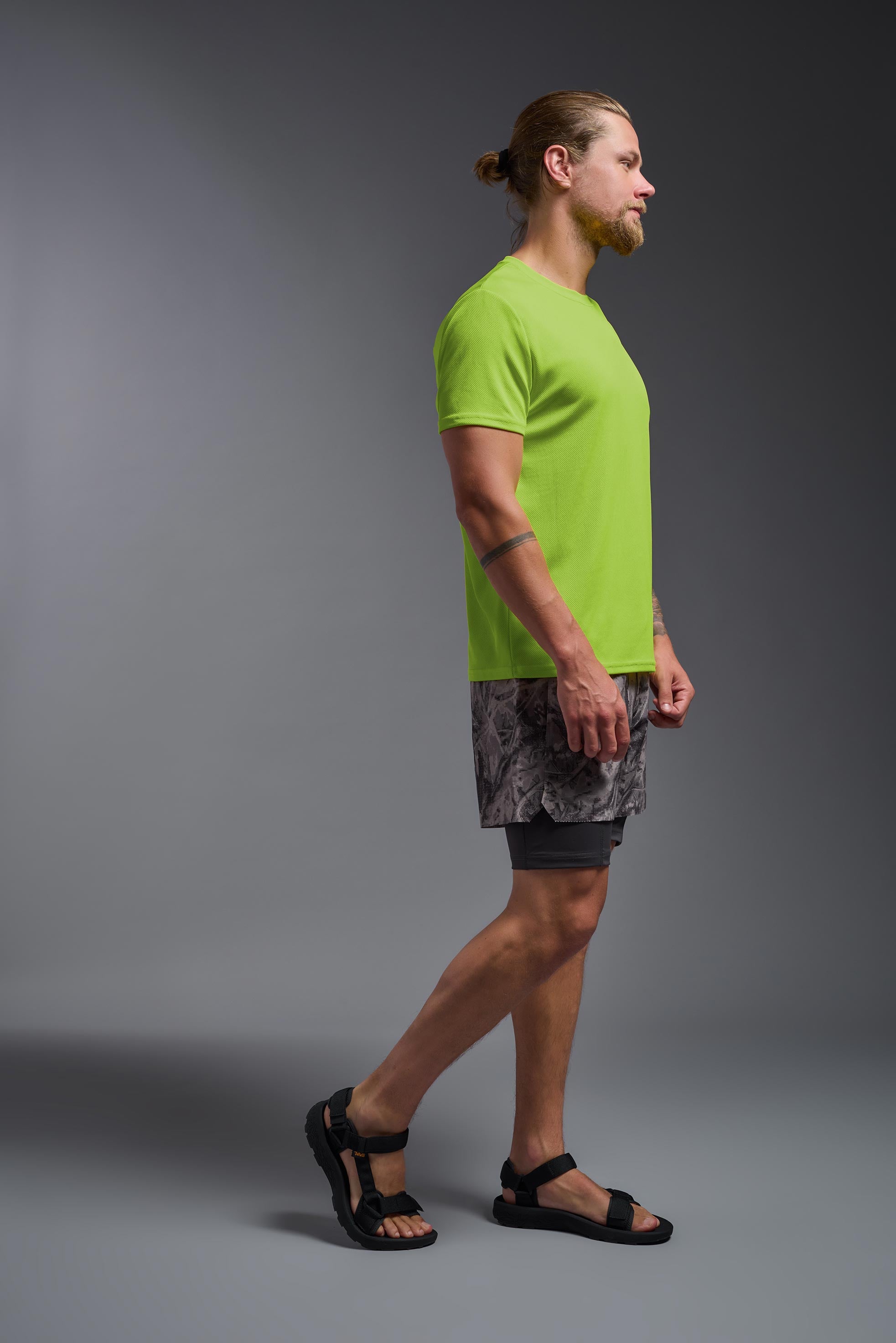 A male model wearing the men's Oxymesh Crewneck Tech Tee Imported Version in the color key lime, made out of 100% polyester, showing the relaxed fit from a side view. This shirt is breathable, quick-drying, moisture-wicking, and Imported for a better price on bulk apparel. #key-lime