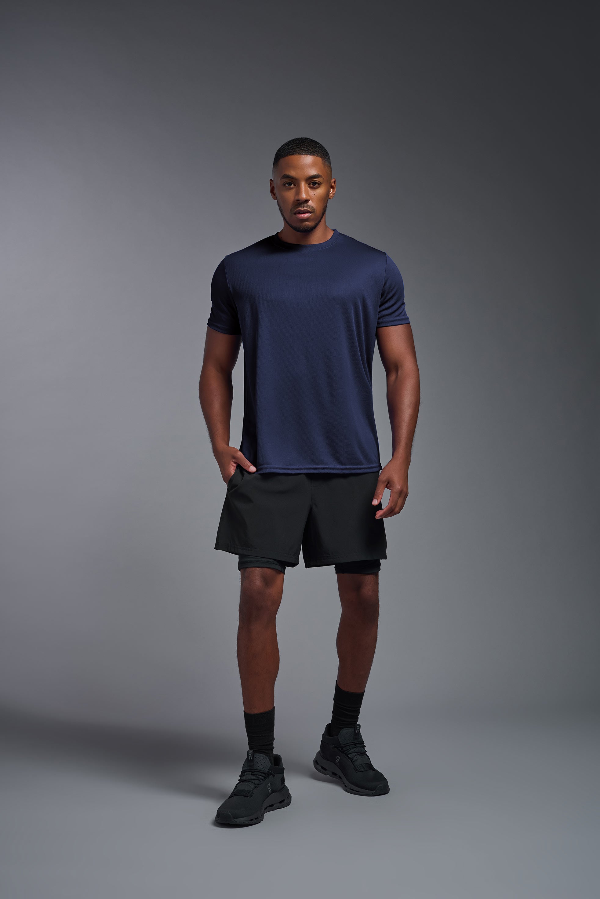 A male model wearing the men's Oxymesh Crewneck Tech Tee Imported Version in the color navy blue, made out of 100% polyester, showing the relaxed fit from a front view. This shirt is breathable, quick-drying, moisture-wicking, and Imported for a better price on bulk apparel. #navy-blue