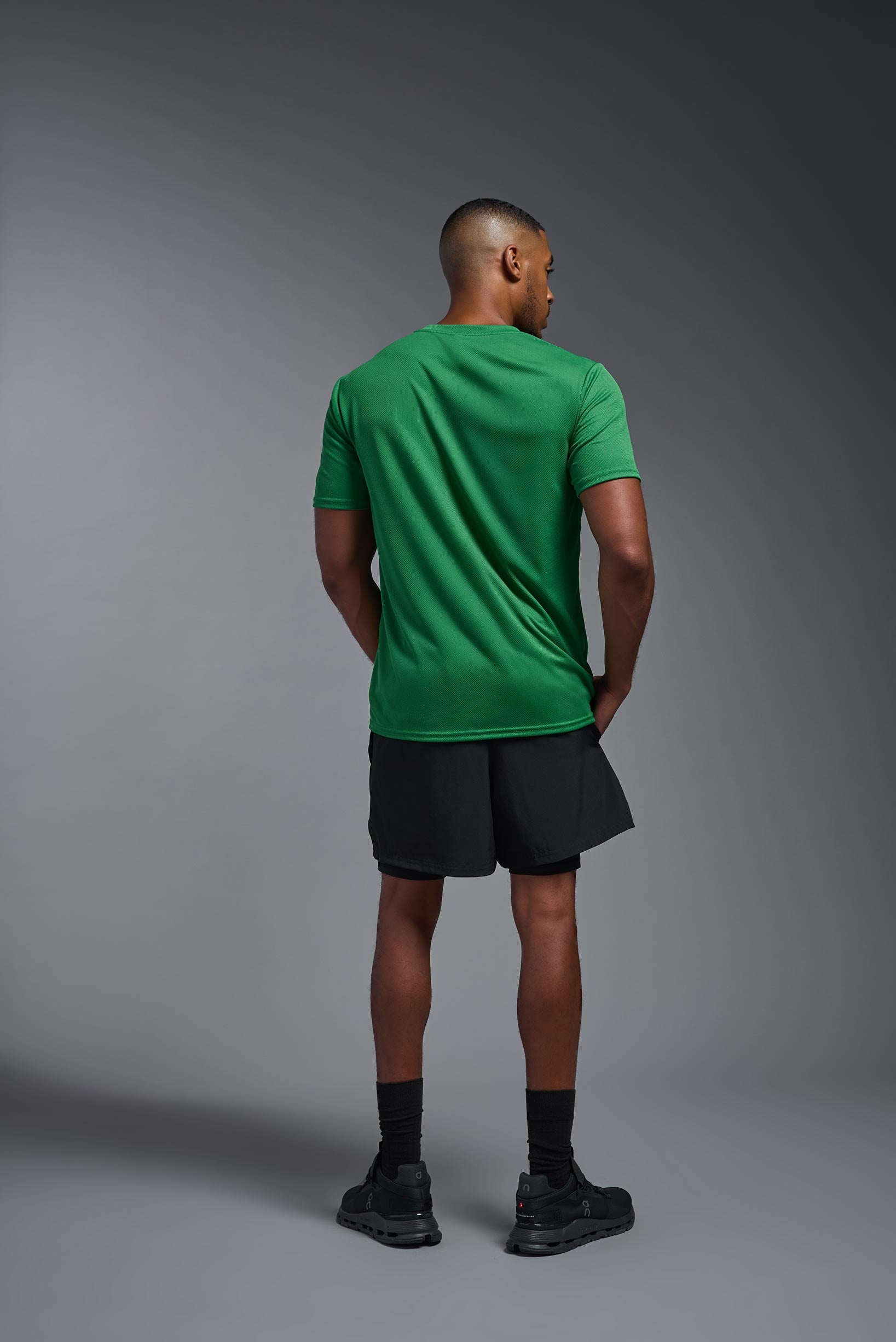 A male model wearing the men's Oxymesh Crewneck Tech Tee in the color kelly green made out of 100% polyester, showing the relaxed fit from a back view. This shirt is breathable, wicks away moisture, quick-dries, and is made in the USA. #kelly-green