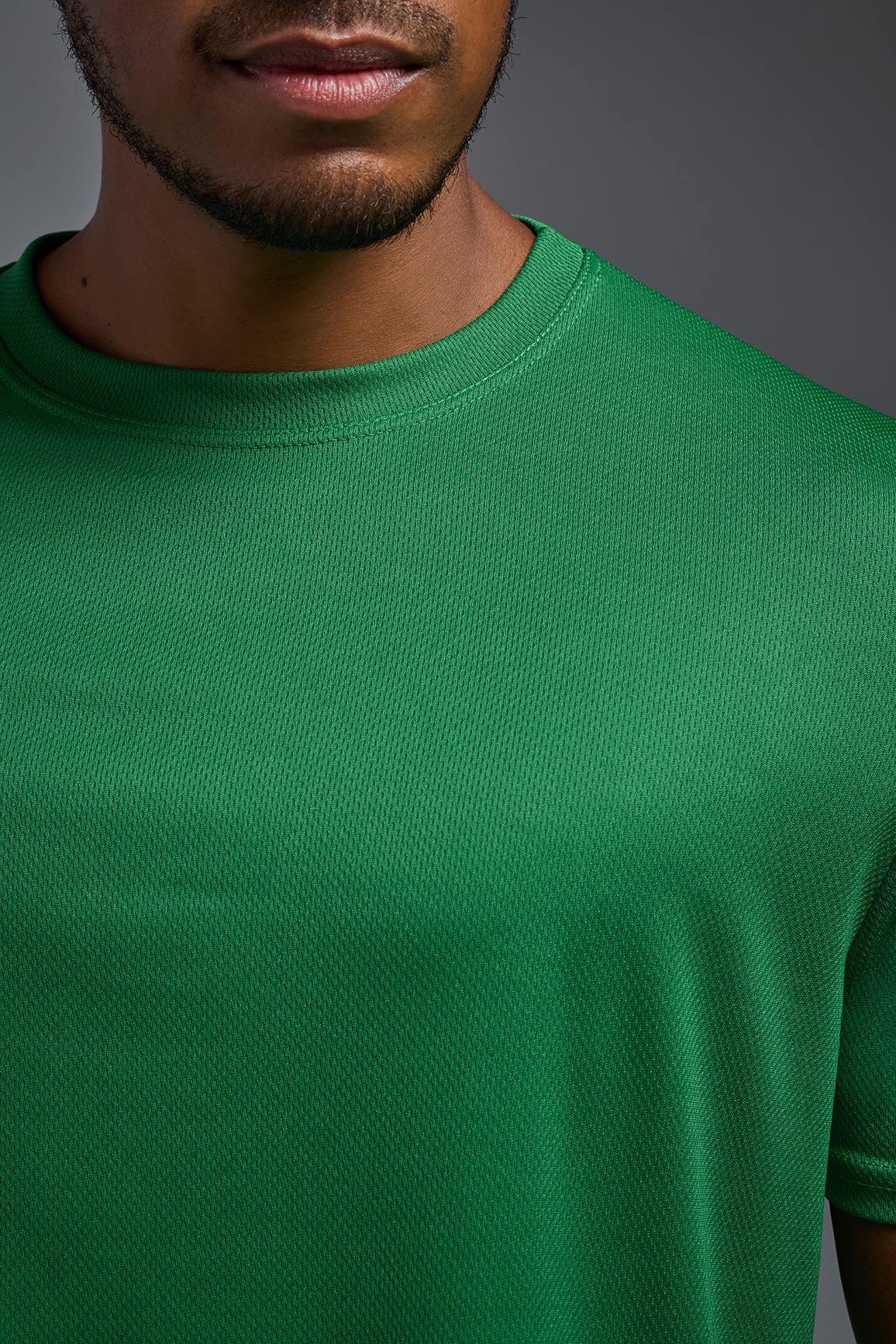 A male model wearing the men's Oxymesh Crewneck Tech Tee in the color kelly green made out of 100% polyester, showing the relaxed fit from a collar close-up view. This shirt is breathable, wicks away moisture, quick-dries, and is made in the USA. #kelly-green