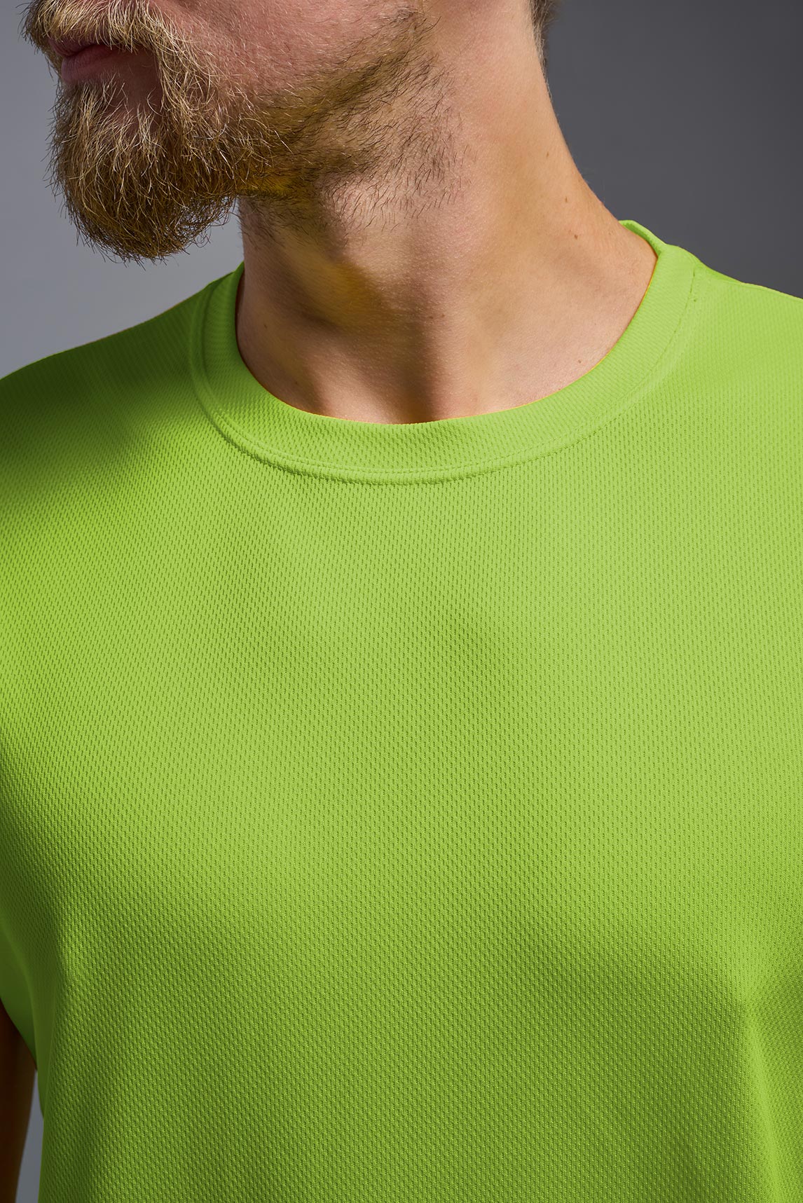 A male model wearing the men's Oxymesh Crewneck Tech Tee in the color key lime made out of 100% polyester, showing the relaxed fit from a front closeup collar view. This shirt is breathable, wicks away moisture, quick-dries, and is made in the USA. #key-lime