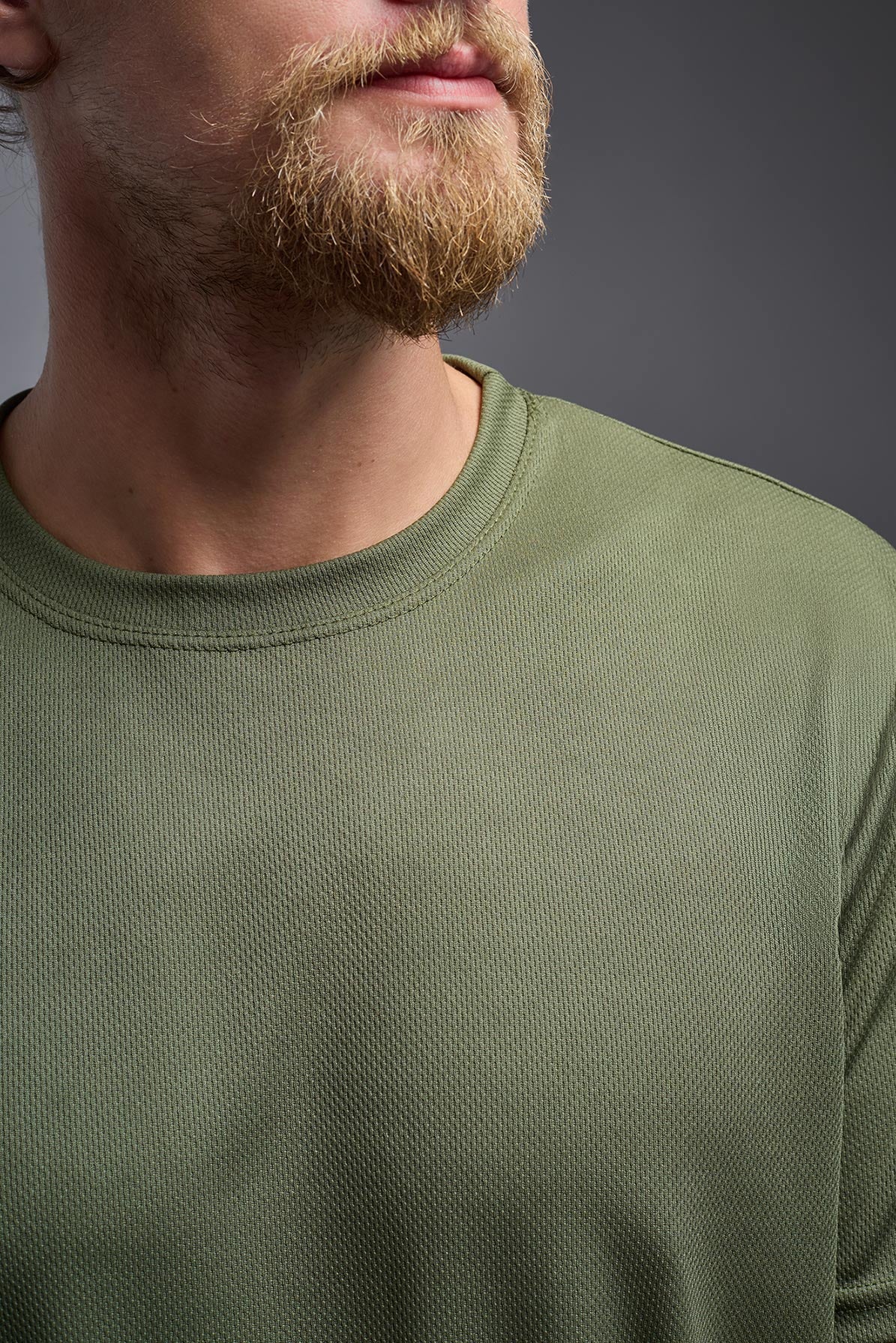 A male model wearing the men's Oxymesh Crewneck Tech Tee in the color military green made out of 100% polyester, showing the relaxed fit from a front close-up collar view. This shirt is breathable, wicks away moisture, quick-dries, and is made in the USA. #military-green