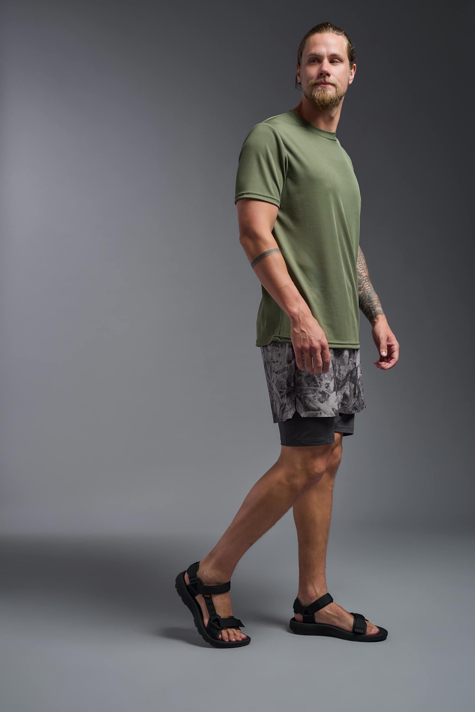 A male model wearing the men's Oxymesh Crewneck Tech Tee in the color military green made out of 100% polyester, showing the relaxed fit from a side view. This shirt is breathable, wicks away moisture, quick-dries, and is made in the USA. #military-green