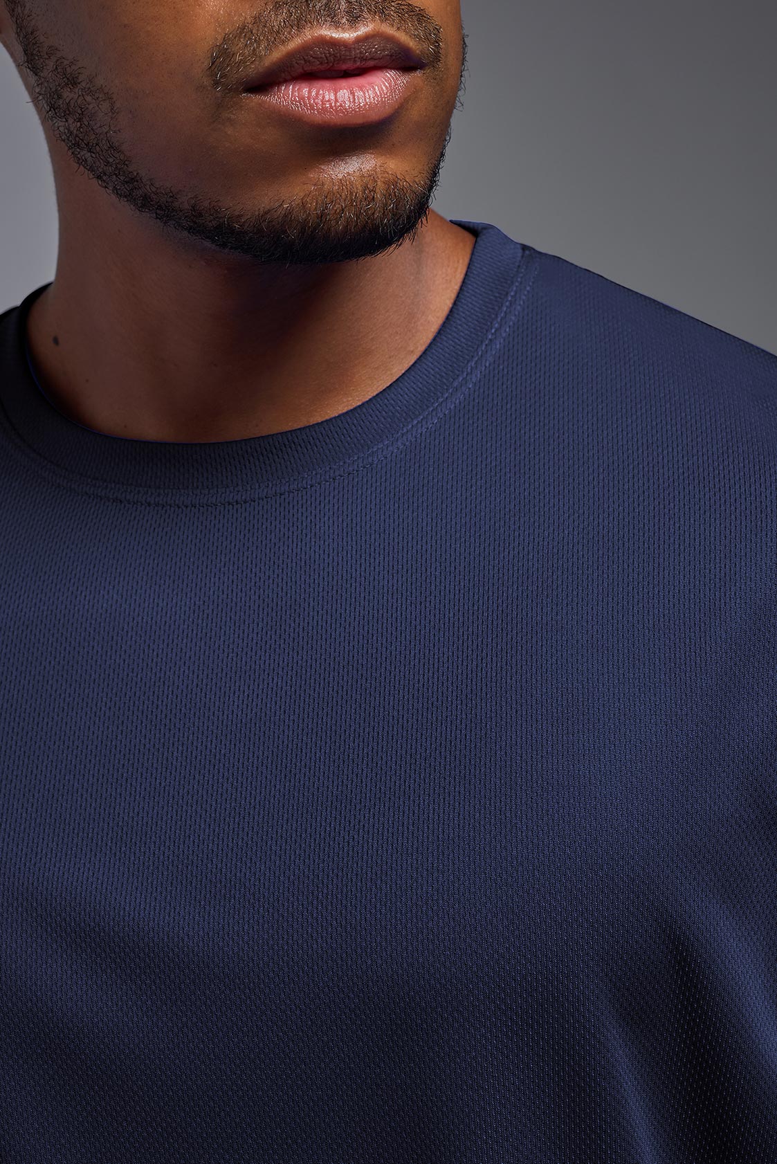 A male model wearing the men's Oxymesh Crewneck Tech Tee in the color navy made out of 100% polyester, showing the relaxed fit from a front closeup collar view. This shirt is breathable, wicks away moisture, quick-dries, and is made in the USA. #navy
