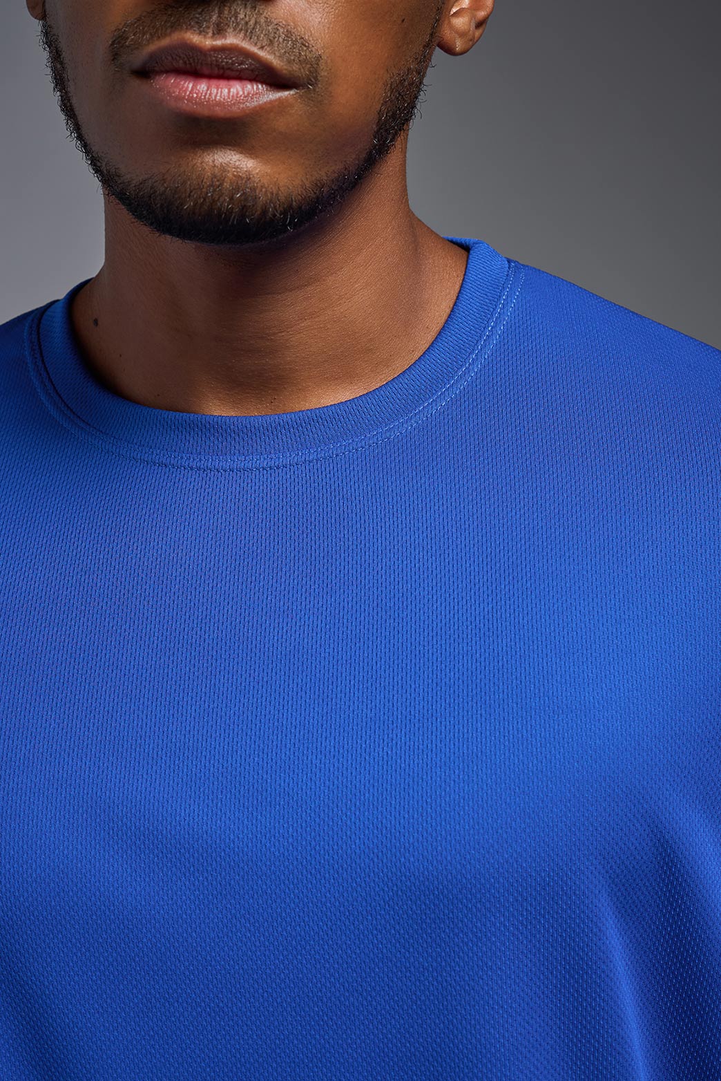 A male model wearing the men's Oxymesh Crewneck Tech Tee in the color royal blue made out of 100% polyester, showing the relaxed fit from a close-up collar view. This shirt is breathable, wicks away moisture, quick-dries, and is made in the USA. #royal-blue