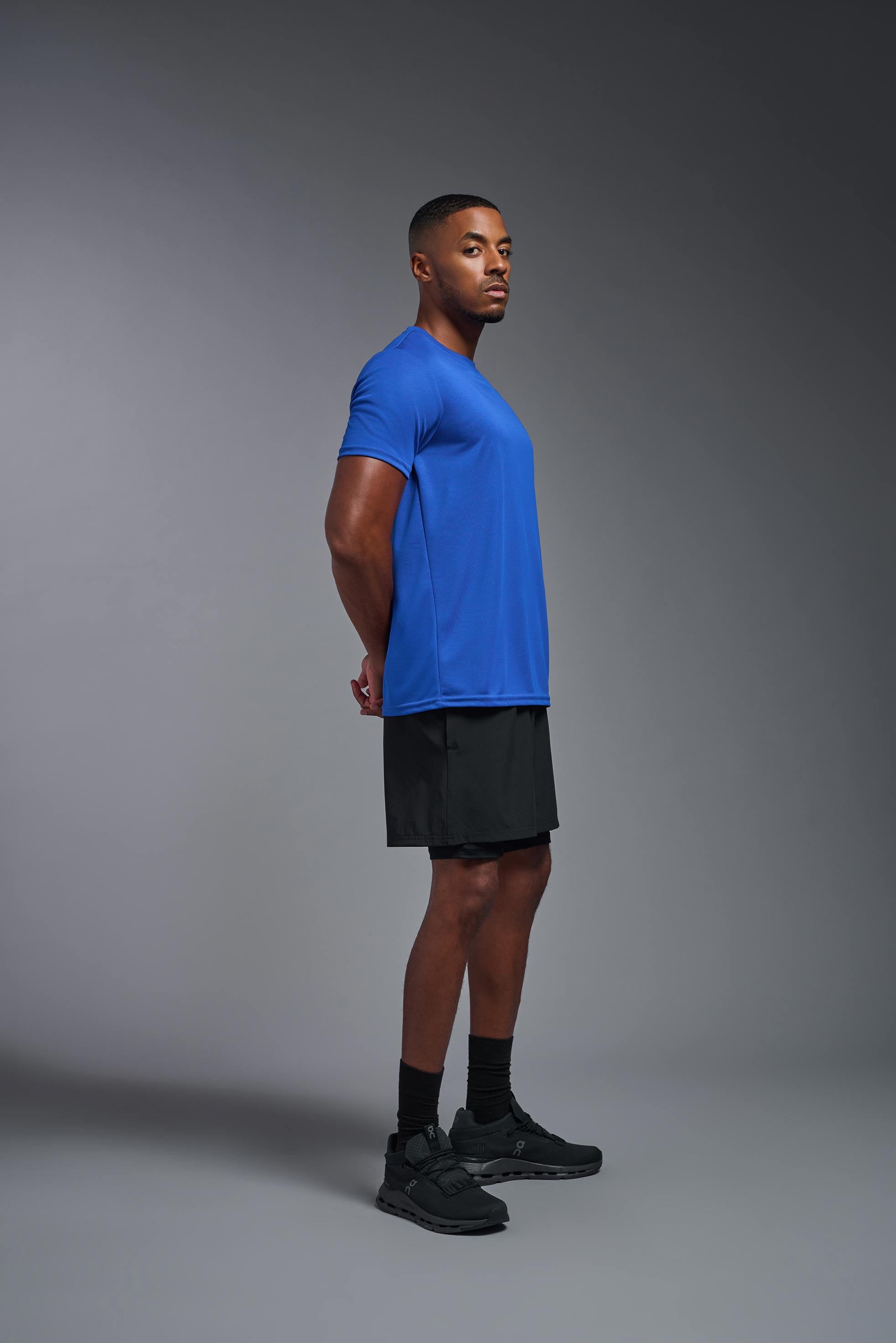 A male model wearing the men's Oxymesh Crewneck Tech Tee in the color royal blue made out of 100% polyester, showing the relaxed fit from a side view. This shirt is breathable, wicks away moisture, quick-dries, and is made in the USA. #royal-blue