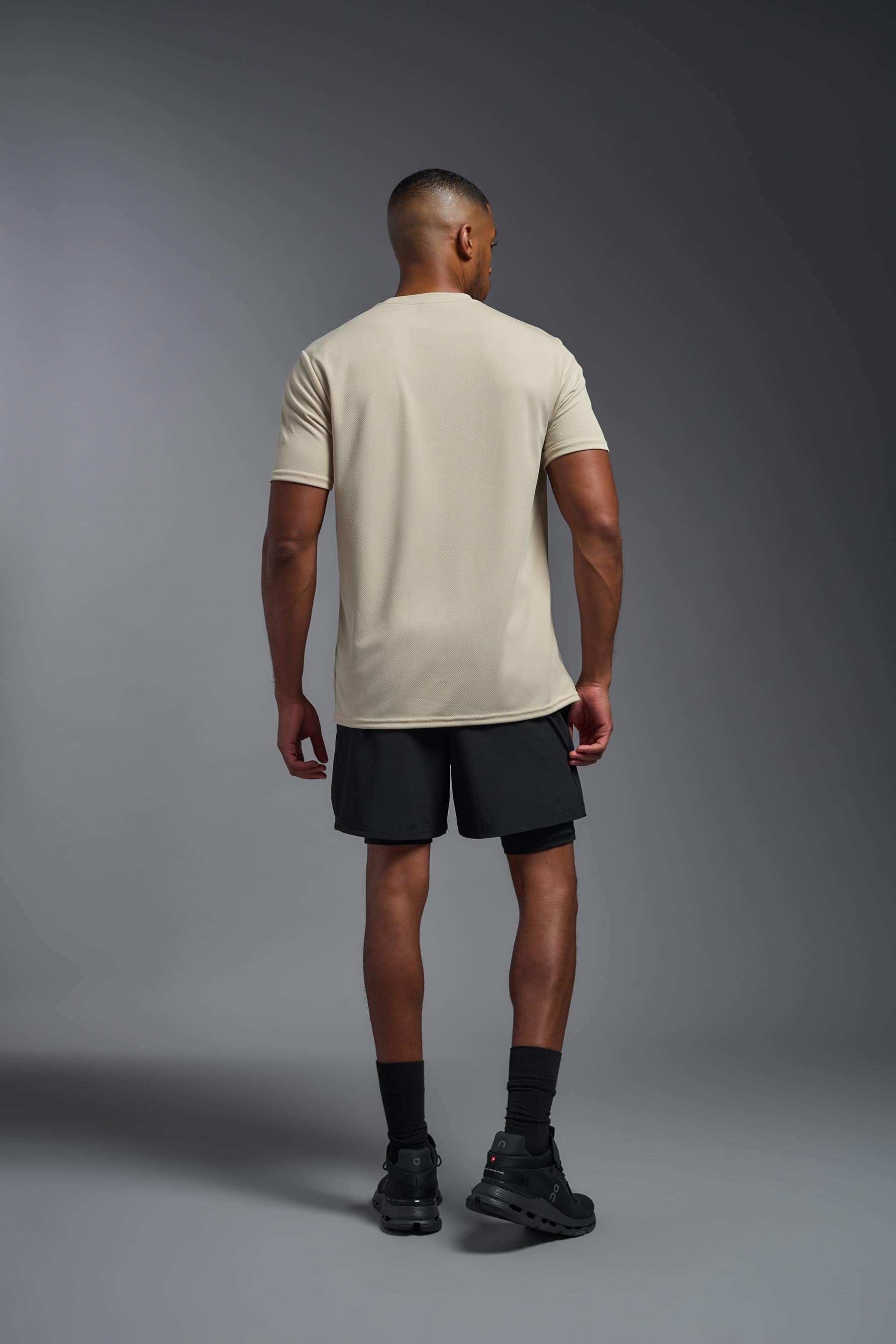 A male model wearing the men's Oxymesh Crewneck Tech Tee in the color sand made out of 100% polyester, showing the relaxed fit from a back view. This shirt is breathable, wicks away moisture, quick-dries, and is made in the USA. #sand
