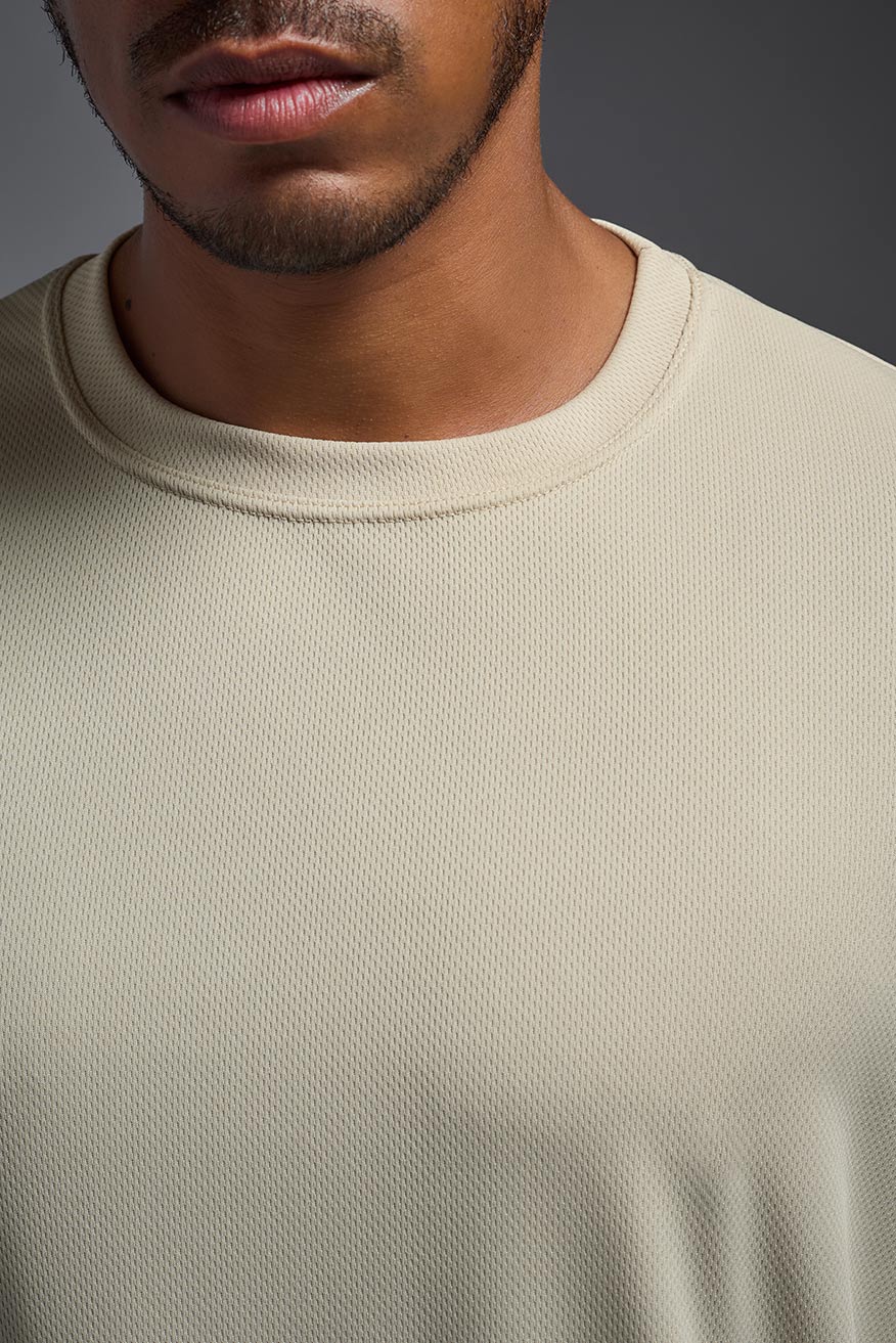 A male model wearing the men's Oxymesh Crewneck Tech Tee in the color sand made out of 100% polyester, showing the relaxed fit from a front view. This shirt is breathable, wicks away moisture, quick-dries, and is made in the USA. #sand