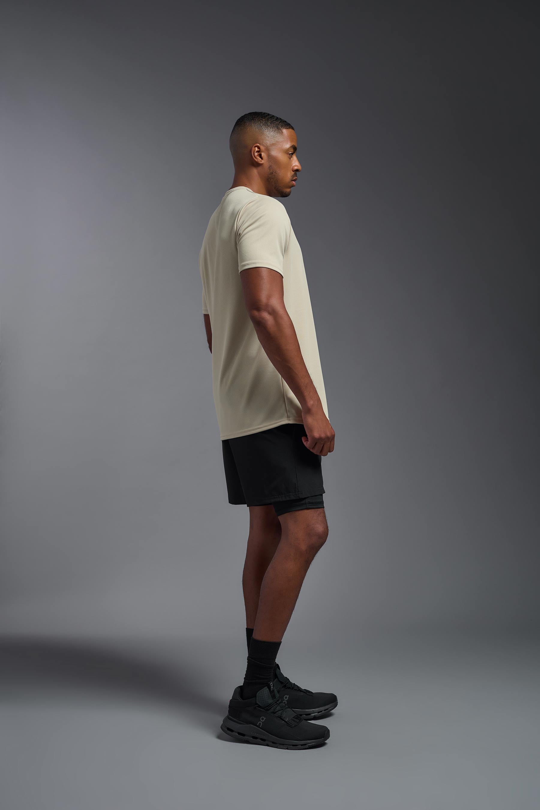 A male model wearing the men's Oxymesh Crewneck Tech Tee in the color sand made out of 100% polyester, showing the relaxed fit from a side view. This shirt is breathable, wicks away moisture, quick-dries, and is made in the USA. #sand