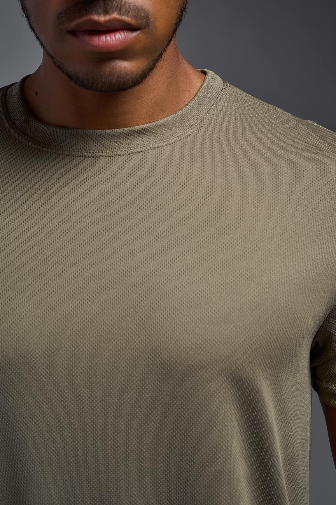 A male model wearing the men's Oxymesh Crewneck Tech Tee in the color tan made out of 100% polyester, showing the relaxed fit from a close-up collar view. This shirt is breathable, wicks away moisture, quick-dries, and is made in the USA. #tan-499