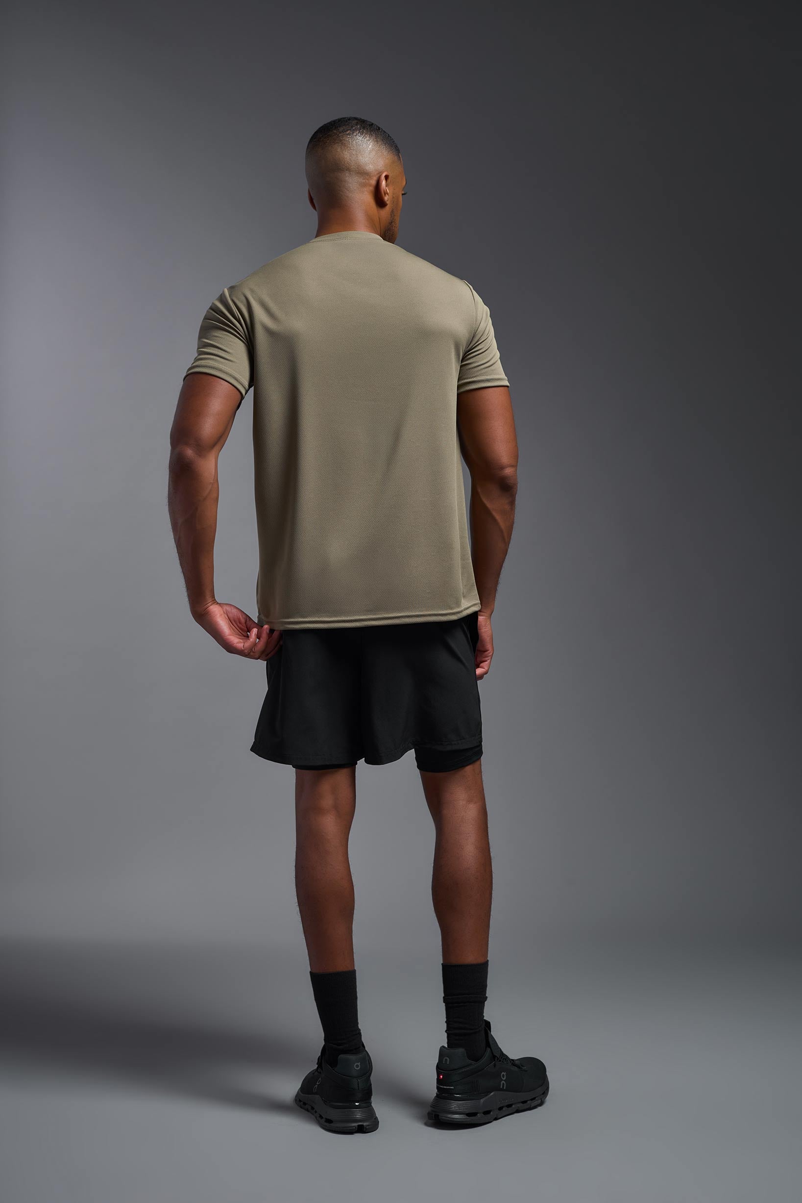 A male model wearing the men's Oxymesh Crewneck Tech Tee in the color tan made out of 100% polyester, showing the relaxed fit from a back view. This shirt is breathable, wicks away moisture, quick-dries, and is made in the USA. #tan