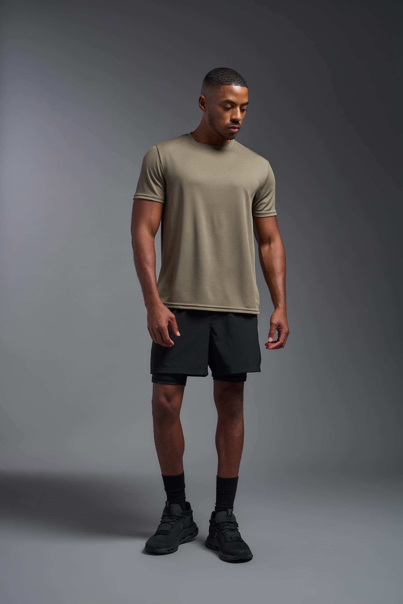 A male model wearing the men's Oxymesh Crewneck Tech Tee in the color tan made out of 100% polyester, showing the relaxed fit from a tan view. This shirt is breathable, wicks away moisture, quick-dries, and is made in the USA. #tan