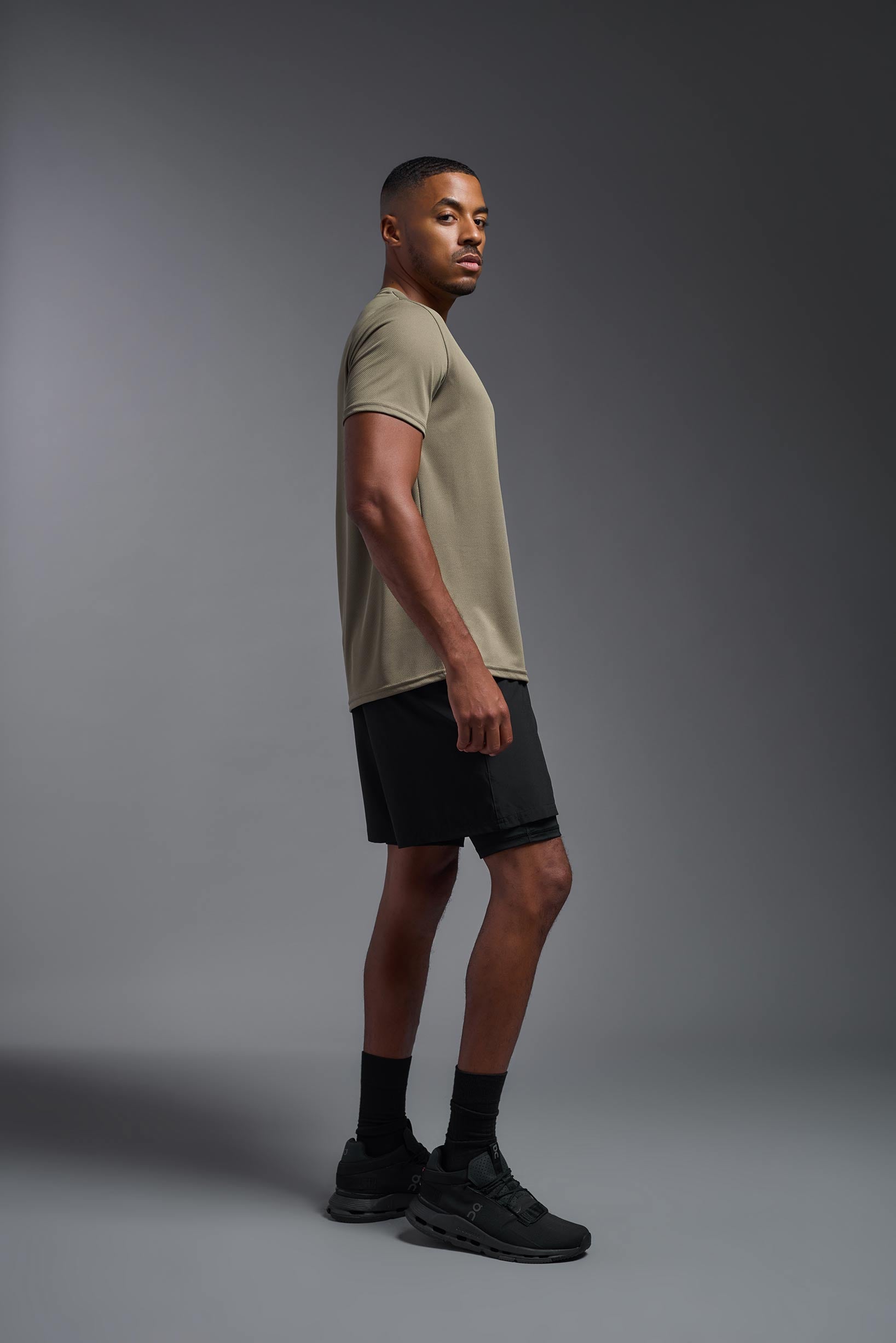 A male model wearing the men's Oxymesh Crewneck Tech Tee in the color tan made out of 100% polyester, showing the relaxed fit from a side view. This shirt is breathable, wicks away moisture, quick-dries, and is made in the USA. #tan
