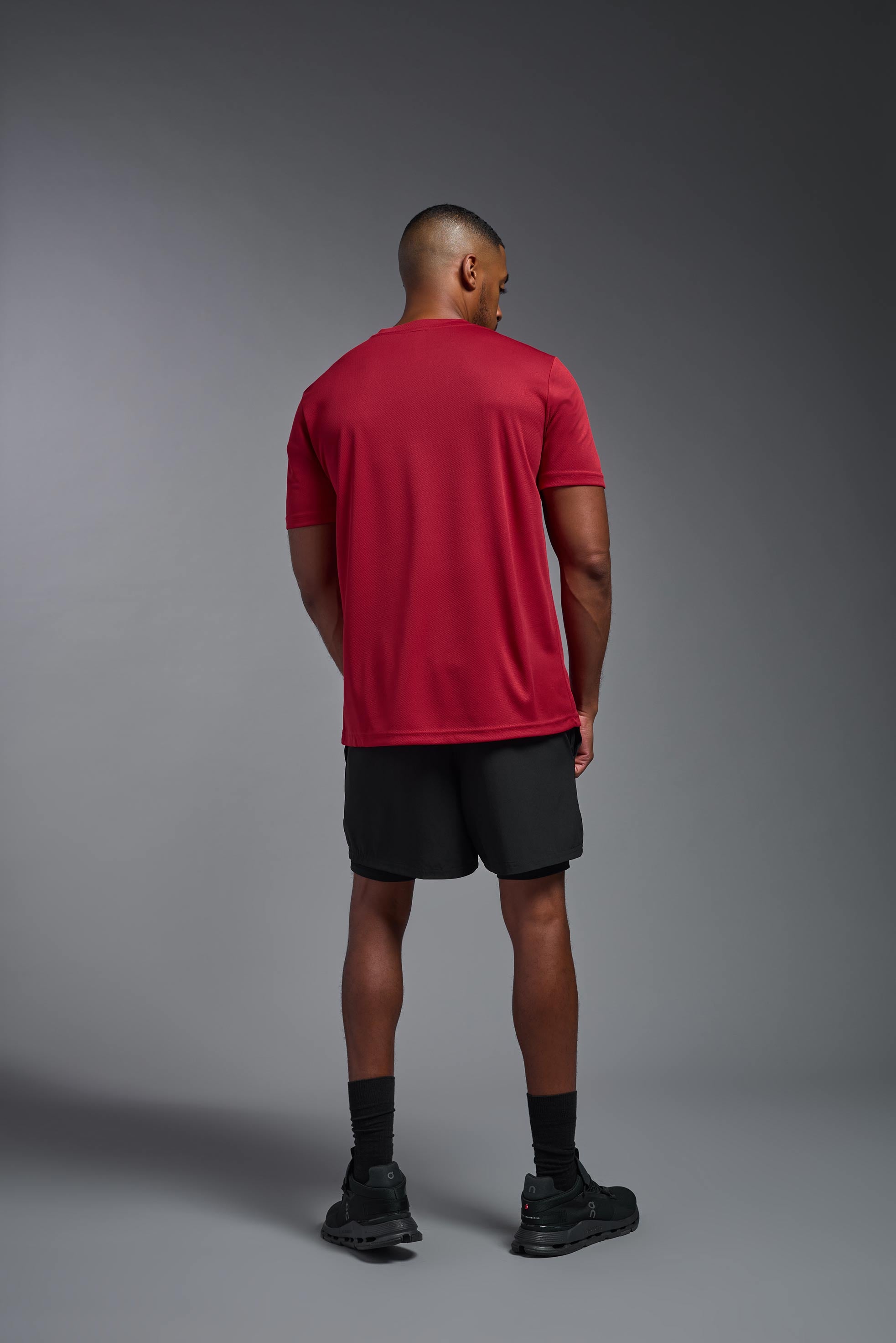 A male model wearing the men's Oxymesh Crewneck Tech Tee in the color true red made out of 100% polyester, showing the relaxed fit from a back view. This shirt is breathable, wicks away moisture, quick-dries, and is made in the USA. #true-red