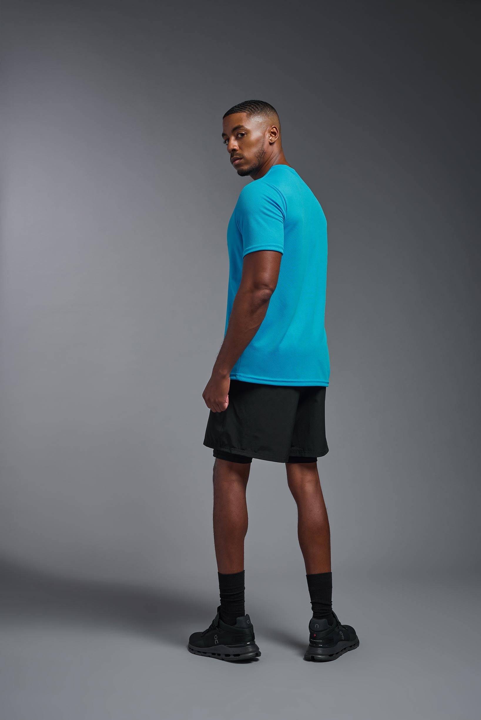 A male model wearing the men's Oxymesh Crewneck Tech Tee in the color turquoise made out of 100% polyester, showing the relaxed fit from a turquoise back view. This shirt is breathable, wicks away moisture, quick-dries, and is made in the USA. #turquoise