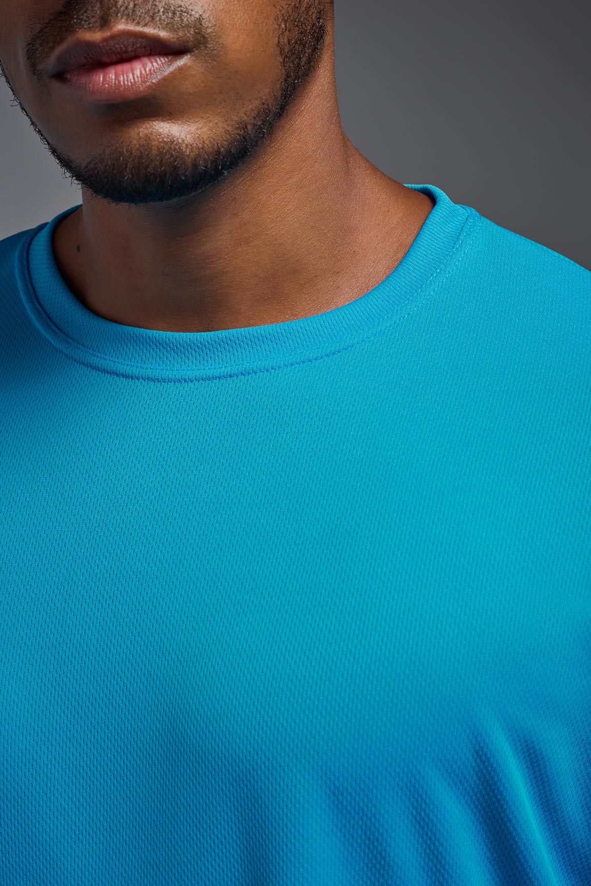 A male model wearing the men's Oxymesh Crewneck Tech Tee in the color turquoise made out of 100% polyester, showing the relaxed fit from a turquoise front collar view. This shirt is breathable, wicks away moisture, quick-dries, and is made in the USA. #turquoise