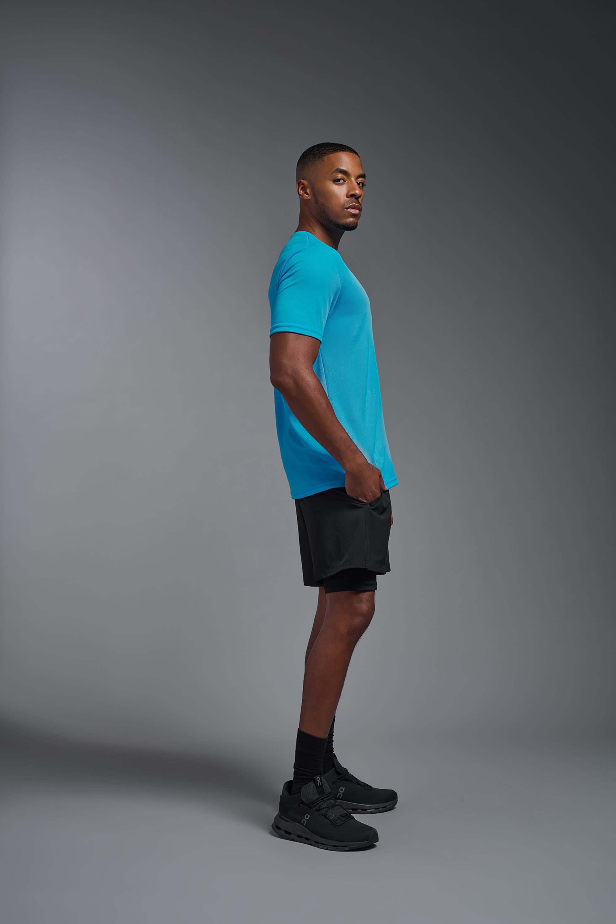 A male model wearing the men's Oxymesh Crewneck Tech Tee in the color turquoise made out of 100% polyester, showing the relaxed fit from a turquoise side view. This shirt is breathable, wicks away moisture, quick-dries, and is made in the USA. #turquoise
