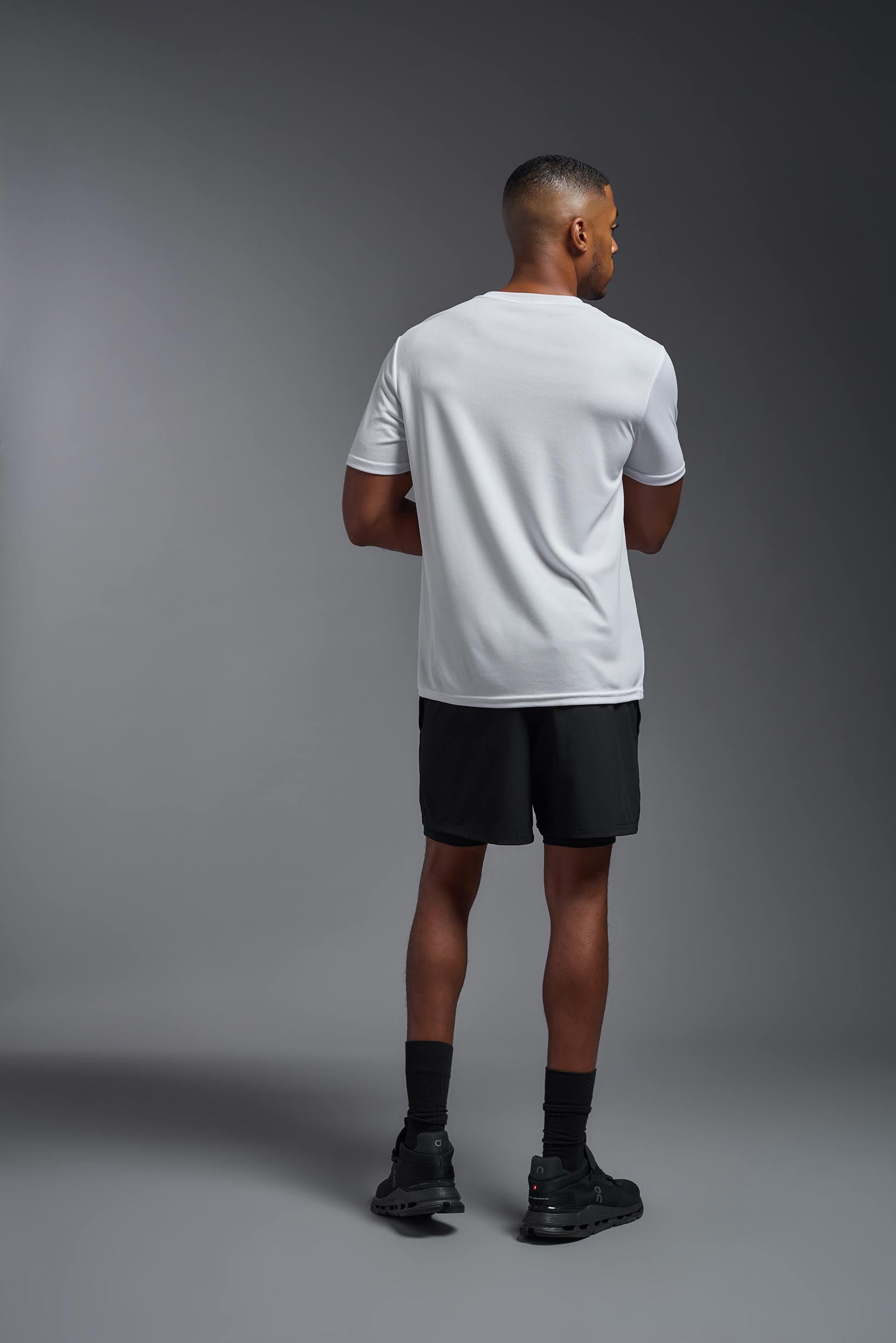 A male model wearing the men's Oxymesh Crewneck Tech Tee in the color white made out of 100% polyester, showing the relaxed fit from a back view. This shirt is breathable, wicks away moisture, quick-dries, and is made in the USA. #white