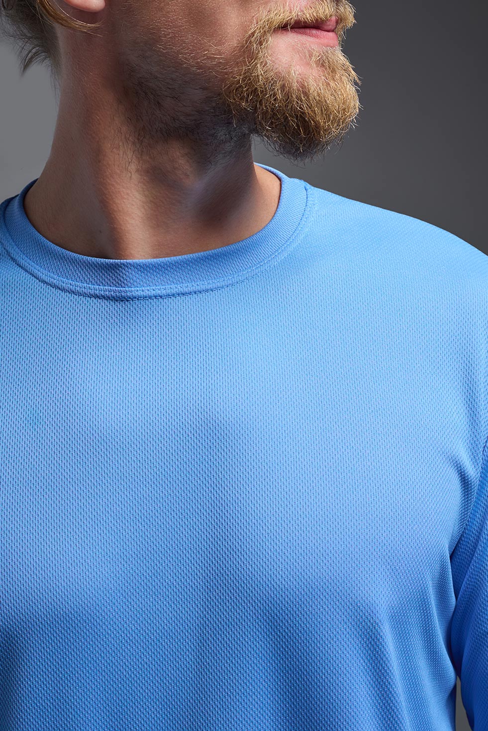 A male model wearing the men's Oxymesh Long Sleeve Tech Tee Imported Version in the color carolina blue, made out of 100% polyester, showing the relaxed fit from a close-up collar view. This shirt is breathable, quick-drying, moisture-wicking, and Imported for a better price on bulk apparel. #carolina-blue