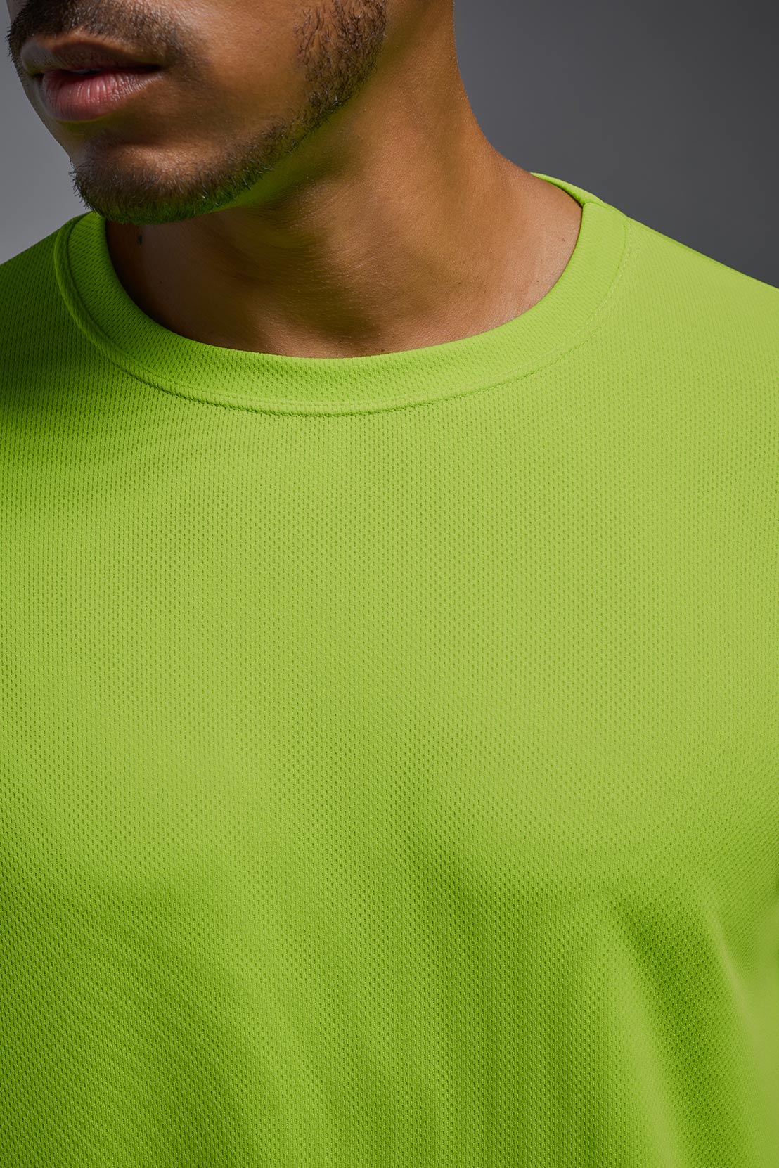 A male model wearing the men's Oxymesh Long Sleeve Tech Tee Imported Version in the color key lime, made out of 100% polyester, showing the relaxed fit from a close-up collar view. This shirt is breathable, quick-drying, moisture-wicking, and Imported for a better price on bulk apparel. #key-lime