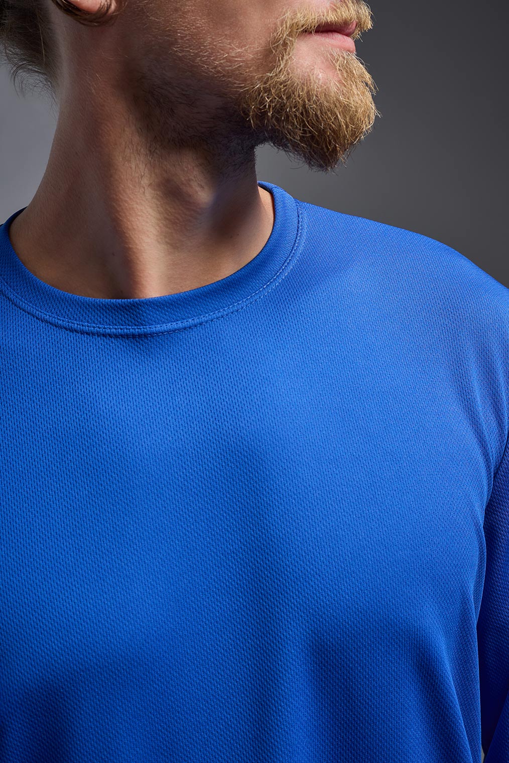 A male model wearing the men's Oxymesh Long Sleeve Tech Tee Imported Version in the color royal blue, made out of 100% polyester, showing the relaxed fit from a close-up collar view. This shirt is breathable, quick-drying, moisture-wicking, and Imported for a better price on bulk apparel. #royal-blue