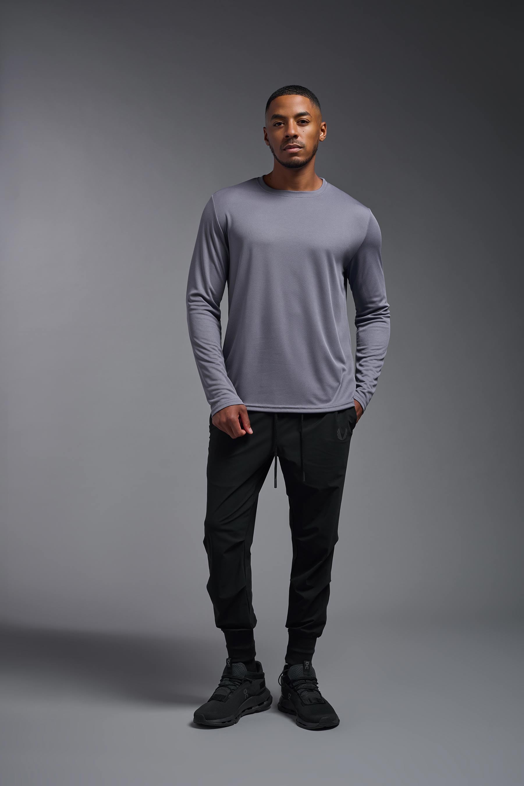A male model wearing the men's Oxymesh Long Sleeve Tech Tee Imported Version in the color steel gray, made out of 100% polyester, showing the relaxed fit from a back view. This shirt is breathable, quick-drying, moisture-wicking, and Imported for a better price on bulk apparel. #steel-gray