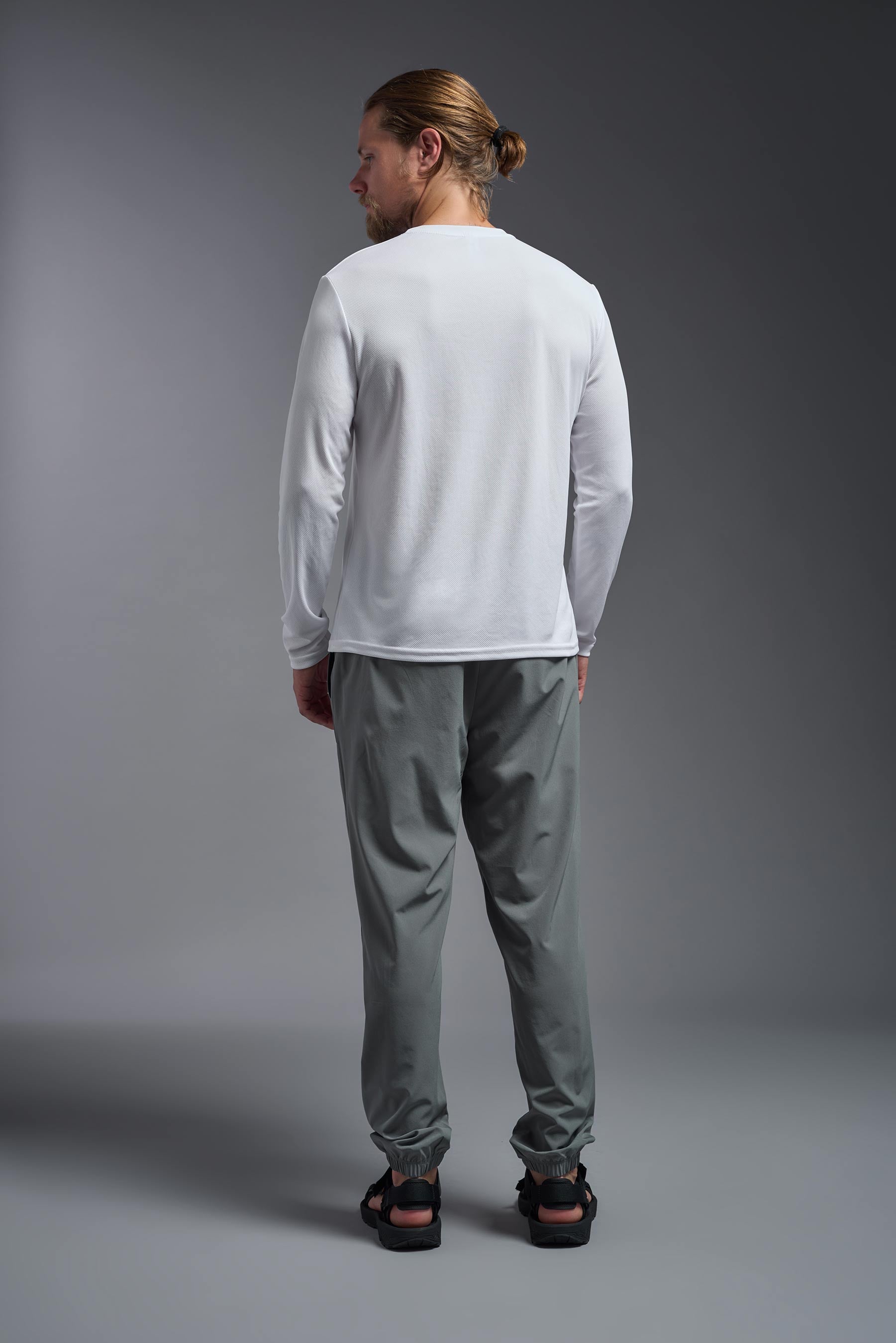 A male model wearing the men's Oxymesh Long Sleeve Tech Tee Imported Version in the color white, made out of 100% polyester, showing the relaxed fit from a back view. This shirt is breathable, quick-drying, moisture-wicking, and Imported for a better price on bulk apparel. #white