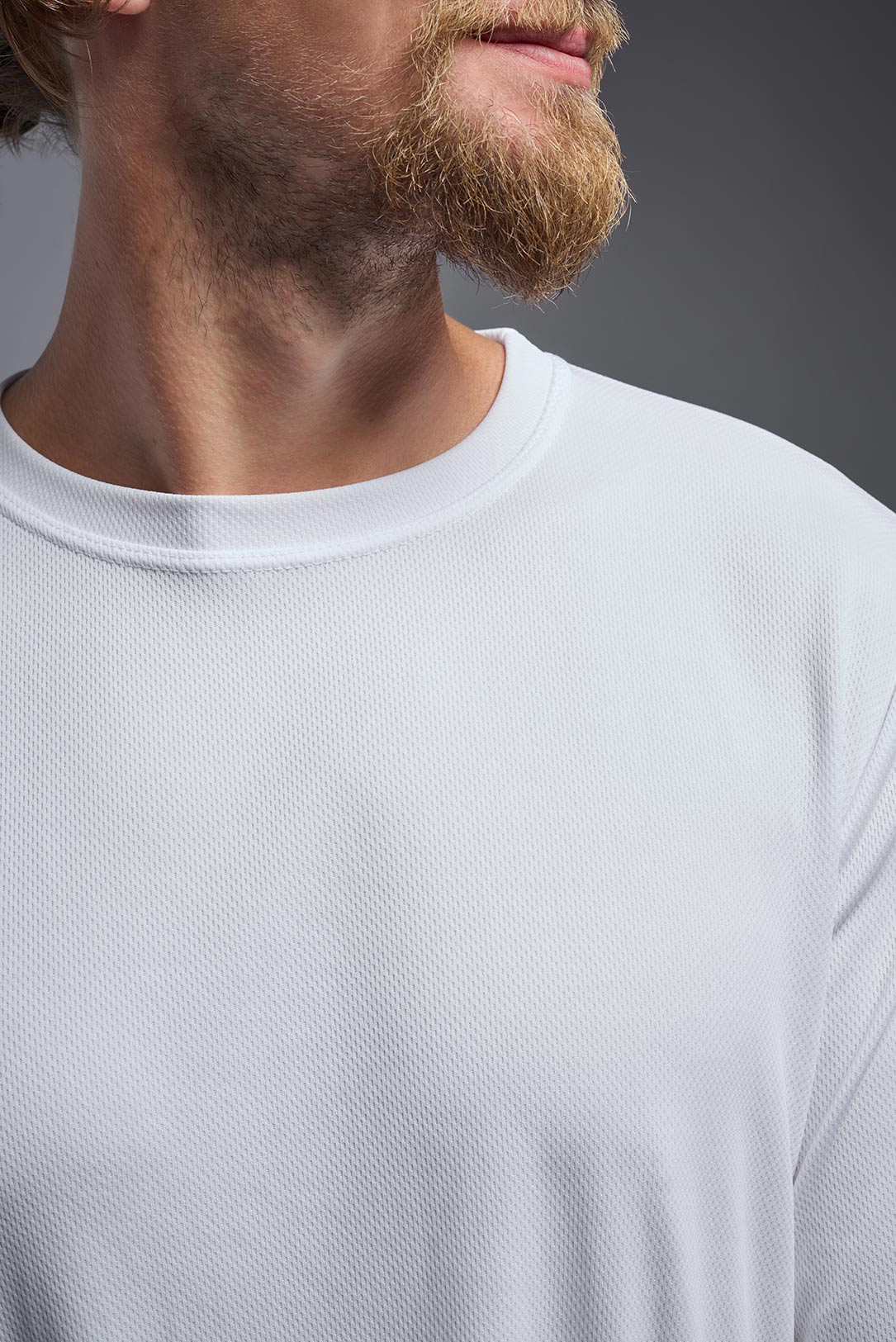 A male model wearing the men's Oxymesh Long Sleeve Tech Tee Imported Version in the color white, made out of 100% polyester, showing the relaxed fit from a close-up collar view. This shirt is breathable, quick-drying, moisture-wicking, and Imported for a better price on bulk apparel. #white