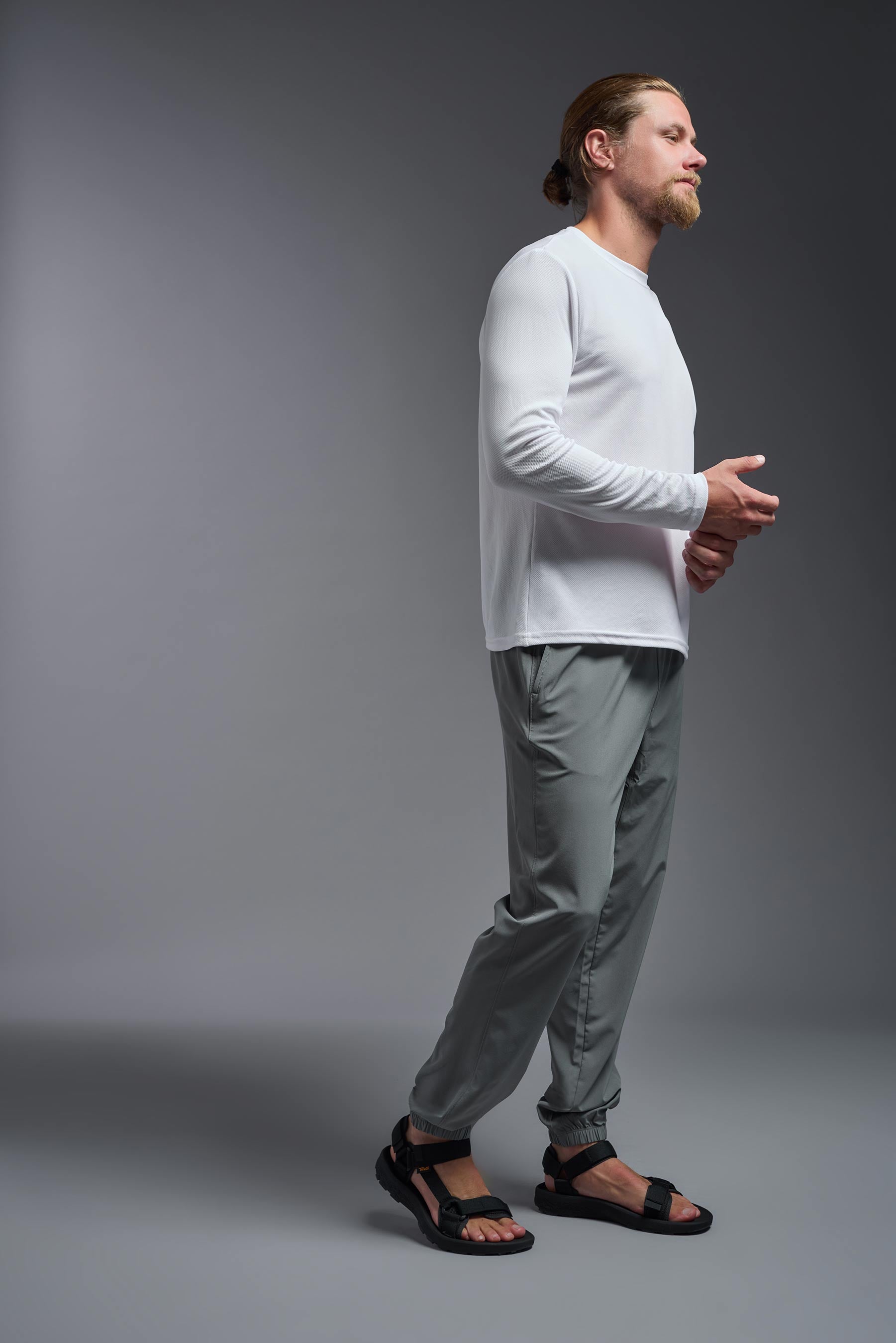 A male model wearing the men's Oxymesh Long Sleeve Tech Tee Imported Version in the color white, made out of 100% polyester, showing the relaxed fit from a side view. This shirt is breathable, quick-drying, moisture-wicking, and Imported for a better price on bulk apparel. #white