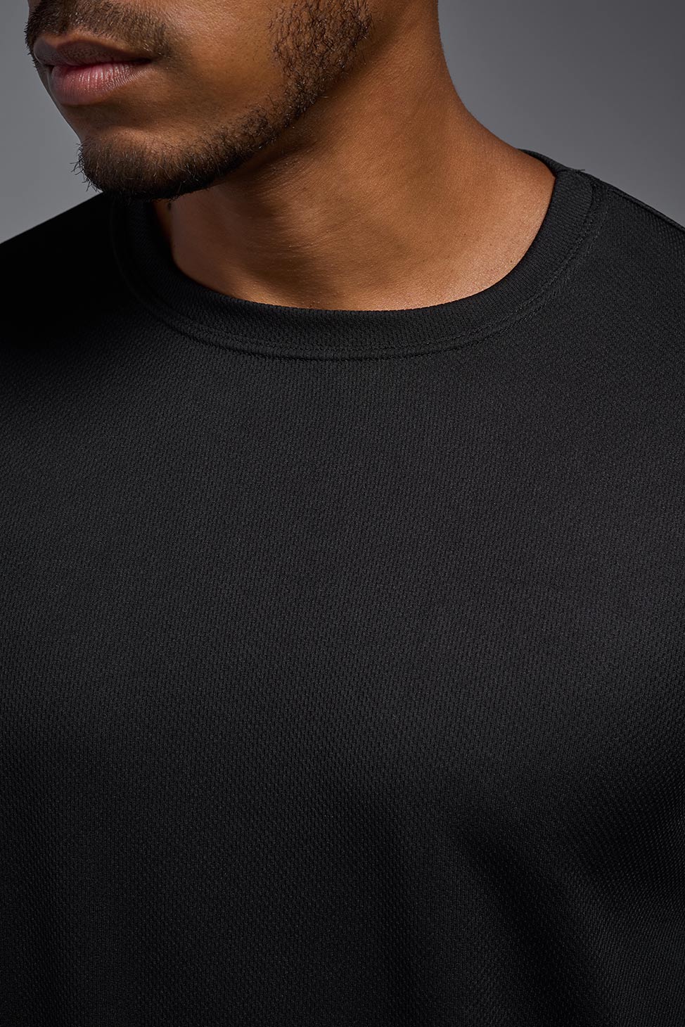 A male model wearing the men's Oxymesh Long Sleeve Tech Tee in the color black, made out of 100% polyester, showing the relaxed fit from a front close-up colllar view. This shirt is breathable, quick-drying, moisture-wicking, and made in the USA. #black