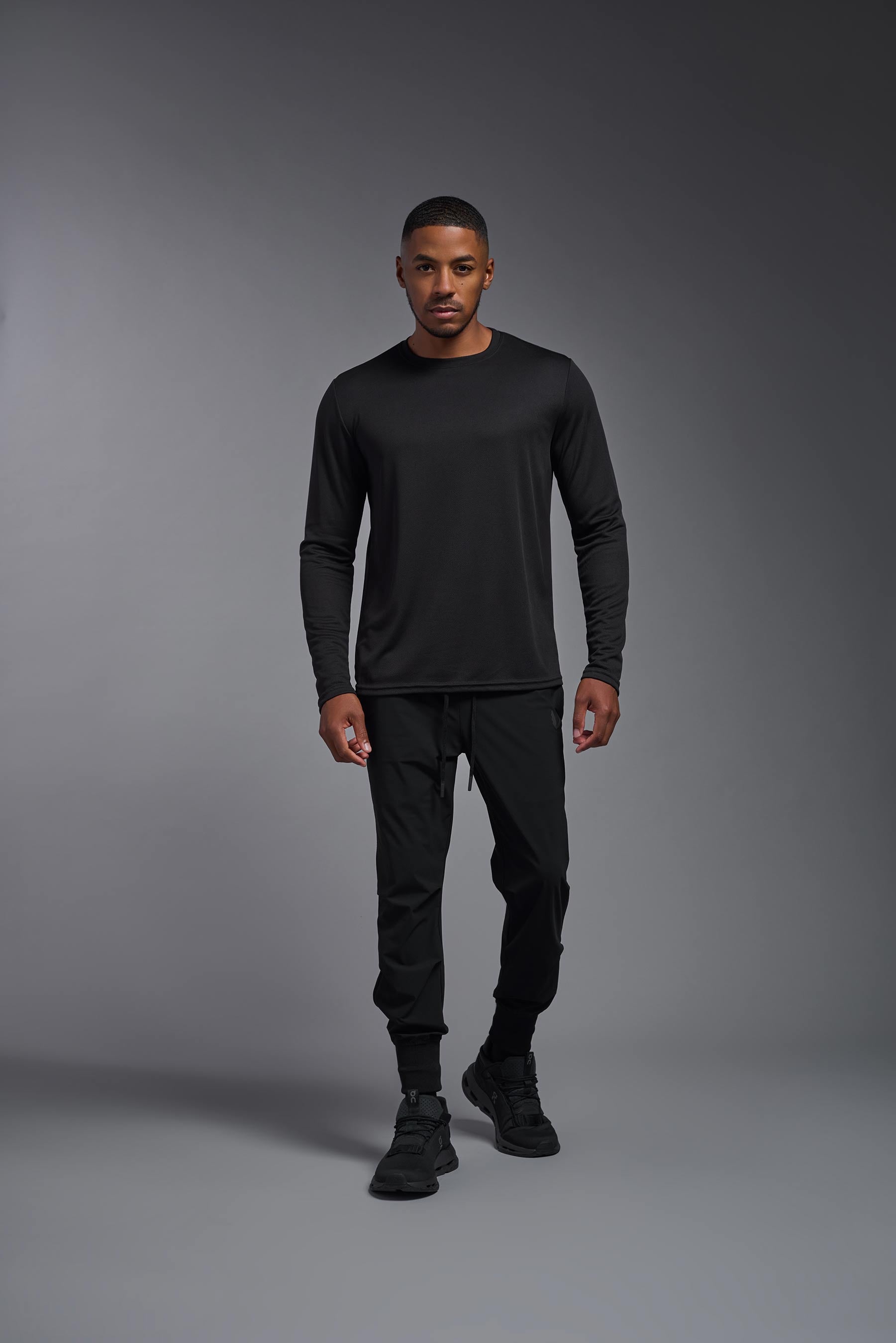 A male model wearing the men's Oxymesh Long Sleeve Tech Tee in the color black, made out of 100% polyester, showing the relaxed fit from a front view. This shirt is breathable, quick-drying, moisture-wicking, and made in the USA. #black