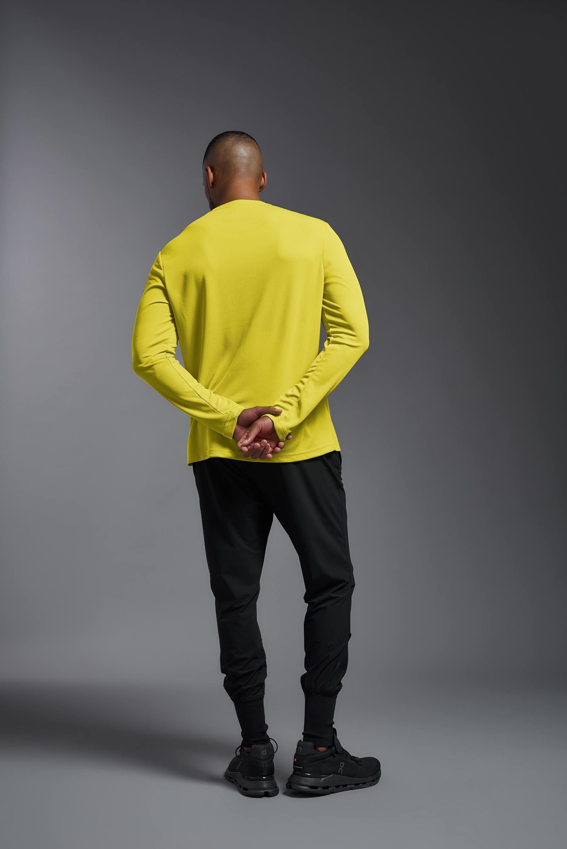 A male model wearing the men's Oxymesh Long Sleeve Tech Tee in the bright yellow made out of 100% polyester, showing the relaxed fit from a back view. This shirt is breathable, quick-drying, moisture-wicking, and made in the USA. #bright-yellow