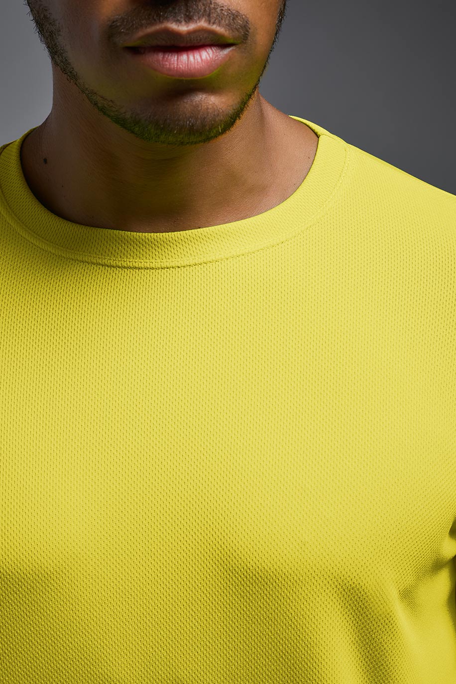 A male model wearing the men's Oxymesh Long Sleeve Tech Tee in the bright yellow made out of 100% polyester, showing the relaxed fit from a collar close-up view. This shirt is breathable, quick-drying, moisture-wicking, and made in the USA. #bright-yellow