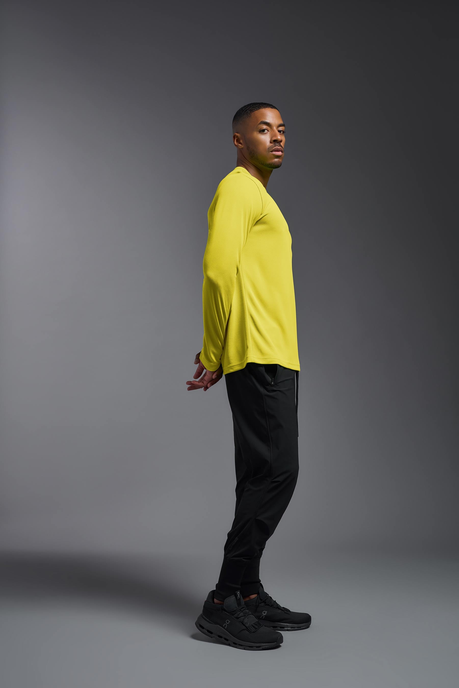 A male model wearing the men's Oxymesh Long Sleeve Tech Tee in the bright yellow made out of 100% polyester, showing the relaxed fit from a side view. This shirt is breathable, quick-drying, moisture-wicking, and made in the USA. #bright-yellow