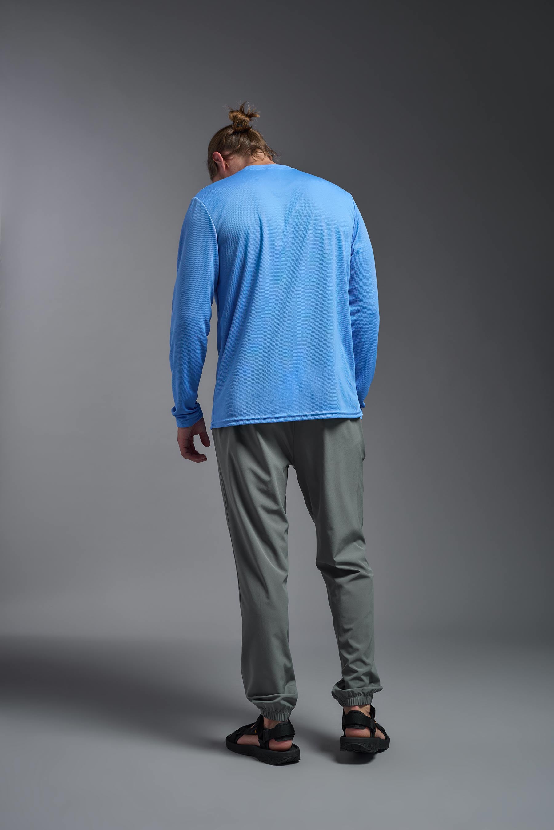 A male model wearing the men's Oxymesh Long Sleeve Tech Tee in the color carolina blue made out of 100% polyester, showing the relaxed fit from a back view. This shirt is breathable, quick-drying, moisture-wicking, and made in the USA. #carolina-blue