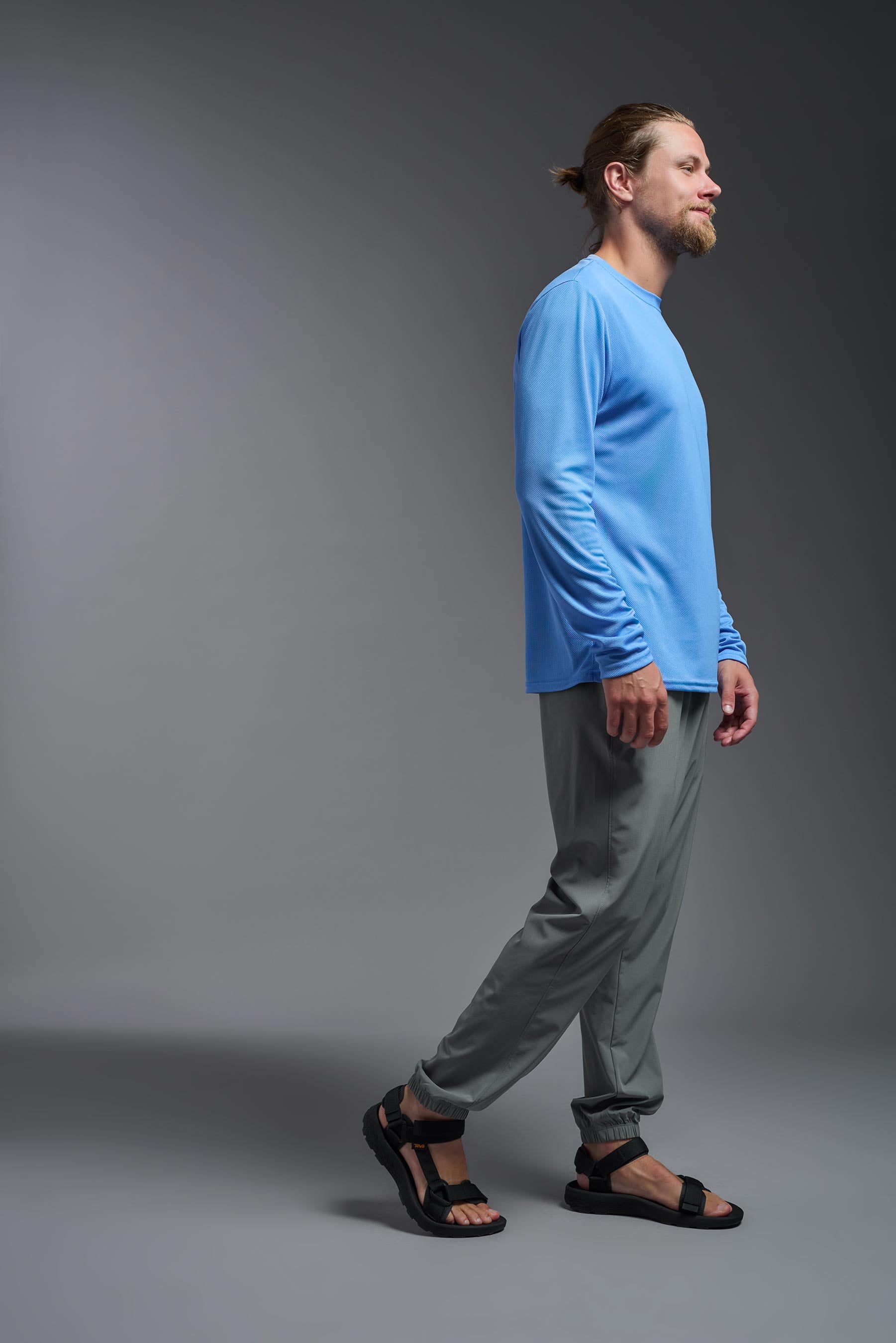 A male model wearing the men's Oxymesh Long Sleeve Tech Tee in the color carolina blue made out of 100% polyester, showing the relaxed fit from a side view. This shirt is breathable, quick-drying, moisture-wicking, and made in the USA. #carolina-blue