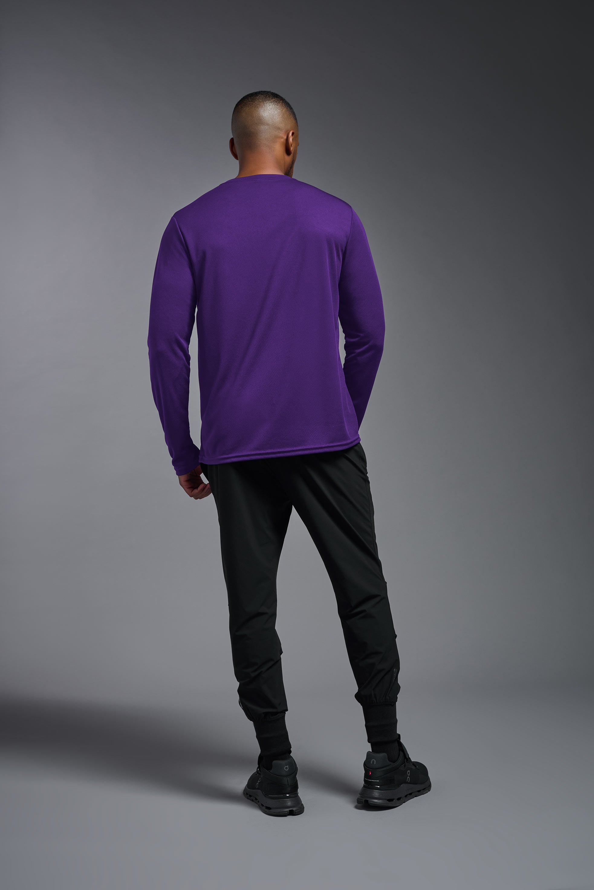 A male model wearing the men's Oxymesh Long Sleeve Tech Tee in the color dark-purple, made out of 100% polyester, showing the relaxed fit from a back view. This shirt is breathable, quick-drying, moisture-wicking, and made in the USA. #dark-purple