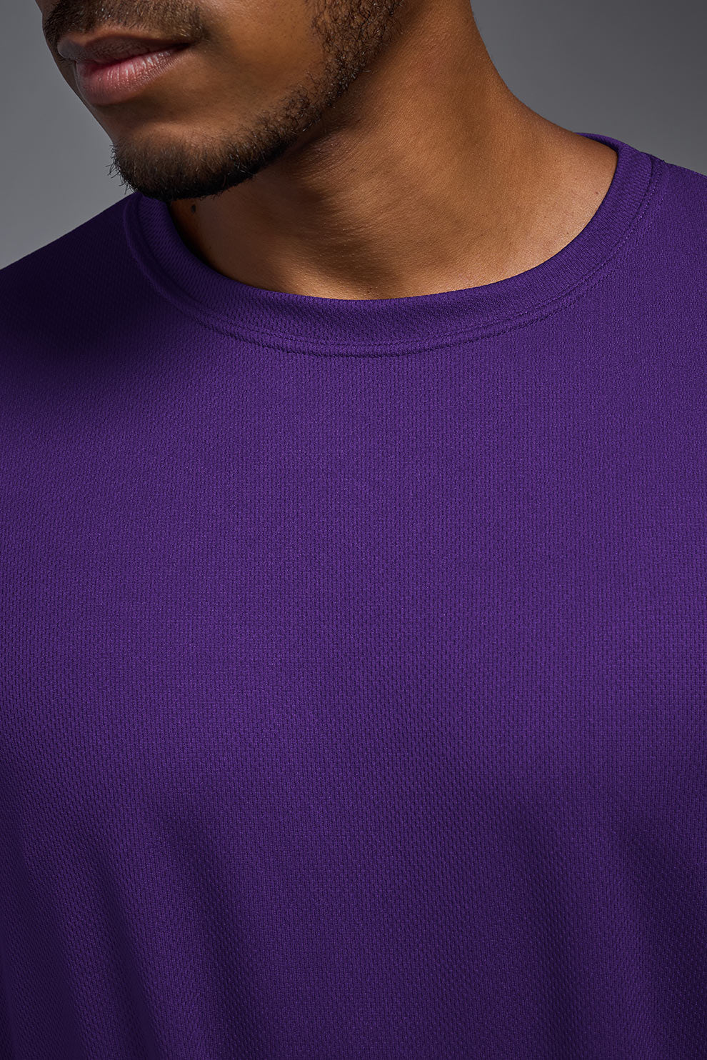 A male model wearing the men's Oxymesh Long Sleeve Tech Tee in the color dark-purple, made out of 100% polyester, showing the relaxed fit from a closeup collar front view. This shirt is breathable, quick-drying, moisture-wicking, and made in the USA. #dark-purple