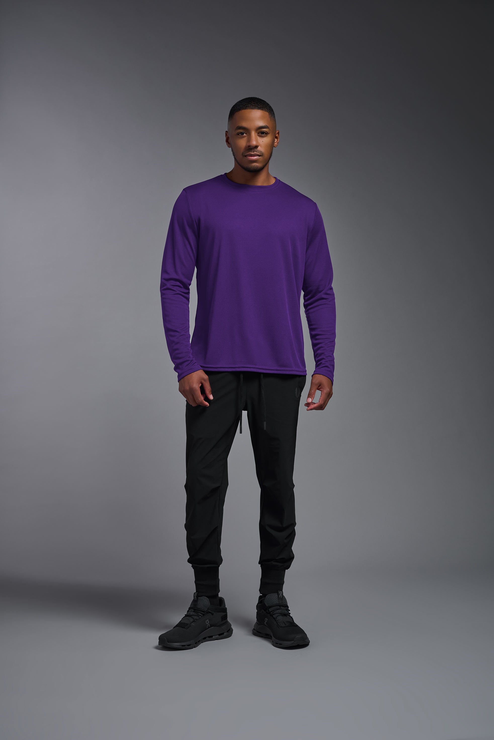 A male model wearing the men's Oxymesh Long Sleeve Tech Tee in the color dark-purple, made out of 100% polyester, showing the relaxed fit from a front view. This shirt is breathable, quick-drying, moisture-wicking, and made in the USA. #dark-purple