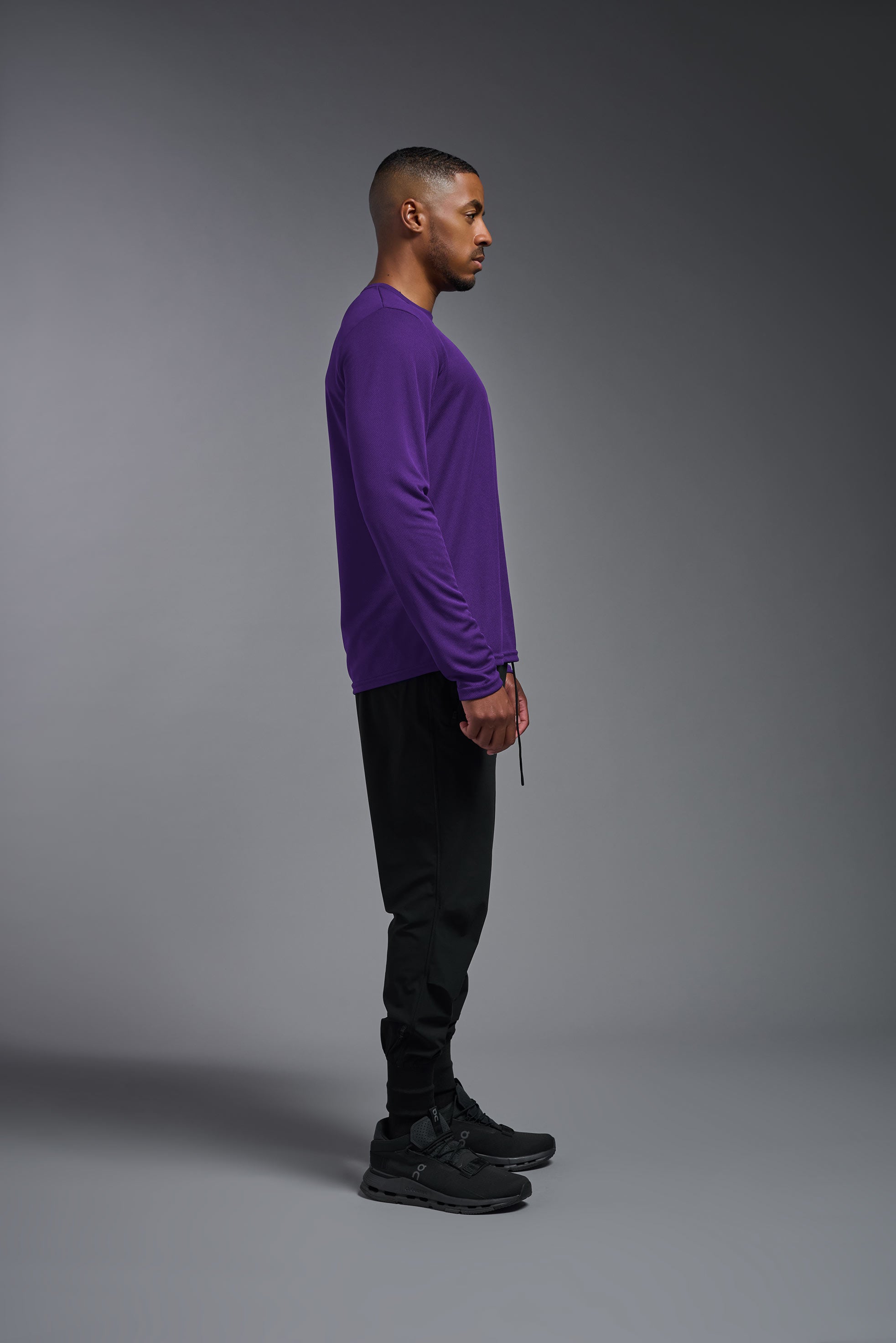 A male model wearing the men's Oxymesh Long Sleeve Tech Tee in the color dark-purple, made out of 100% polyester, showing the relaxed fit from a side view. This shirt is breathable, quick-drying, moisture-wicking, and made in the USA. #dark-purple