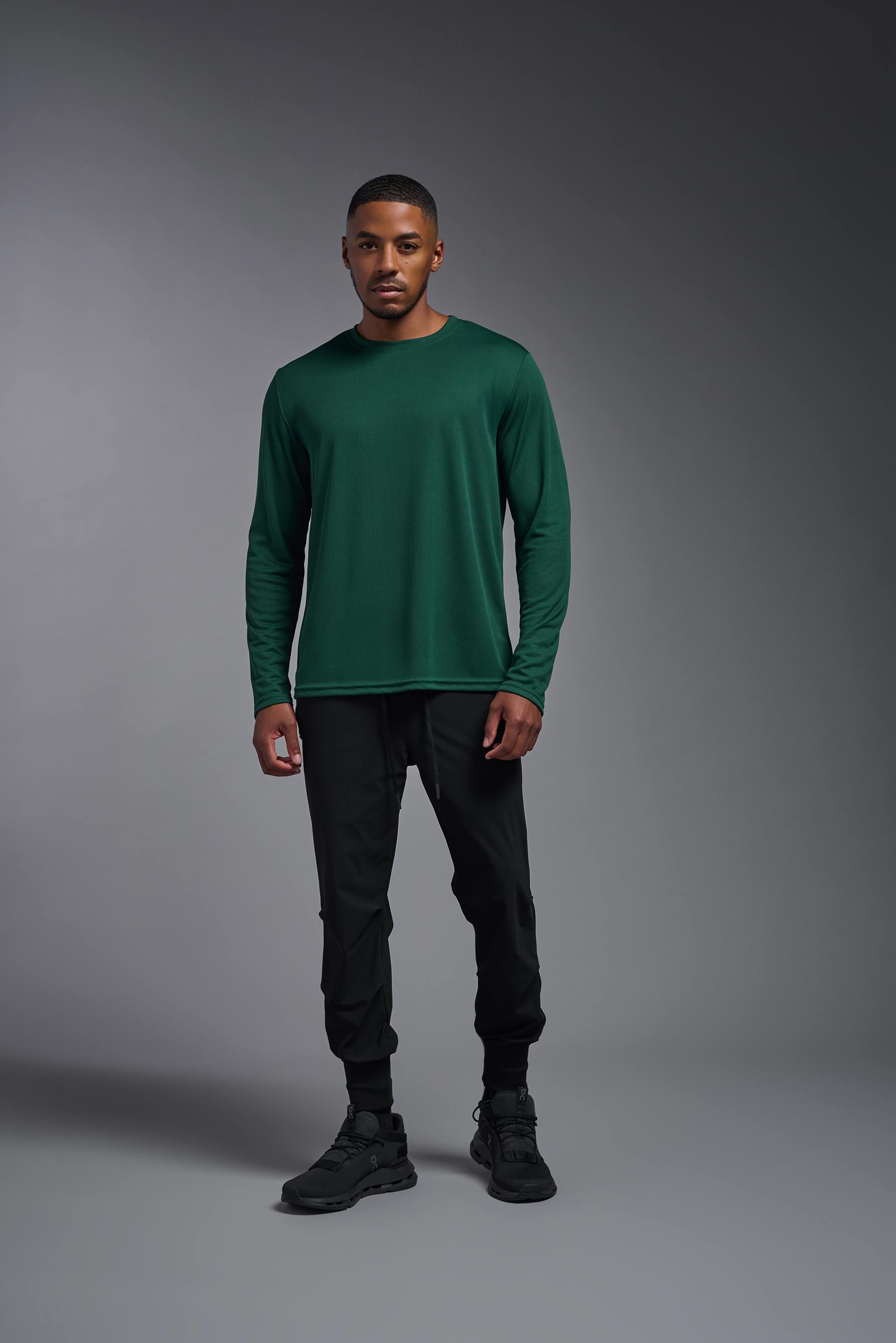 A male model wearing the men's Oxymesh Long Sleeve Tech Tee in the color forest green, made out of 100% polyester, showing the relaxed fit from a front view. This shirt is breathable, quick-drying, moisture-wicking, and made in the USA. #forest-green