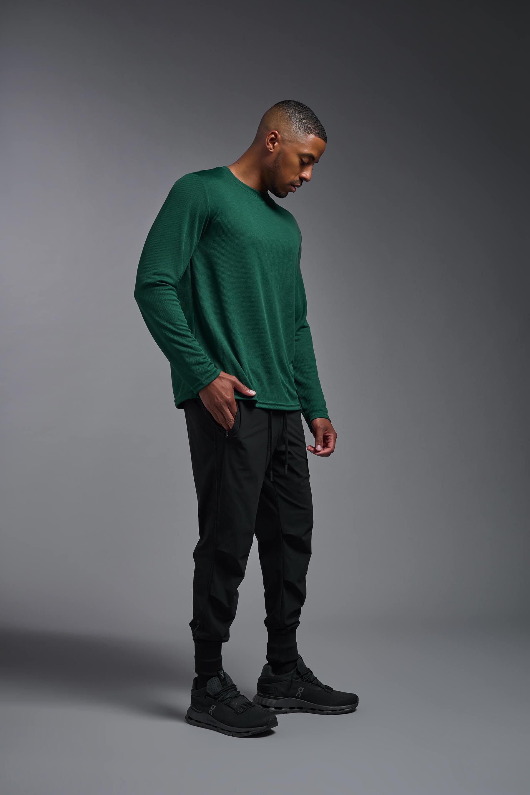 A male model wearing the men's Oxymesh Long Sleeve Tech Tee in the color forest green, made out of 100% polyester, showing the relaxed fit from a side view. This shirt is breathable, quick-drying, moisture-wicking, and made in the USA. #forest-green