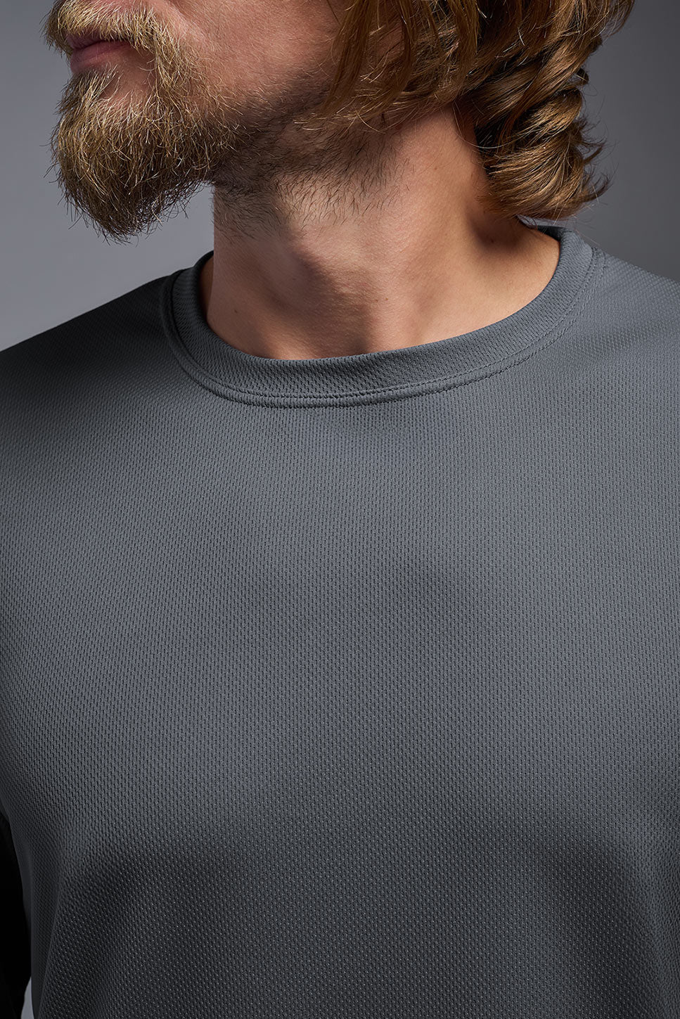 A male model wearing the men's Oxymesh Long Sleeve Tech Tee in the color graphite gray made out of 100% polyester, showing the relaxed fit from a closeup collar view. This shirt is breathable, quick-drying, moisture-wicking, and made in the USA. #graphite-gray