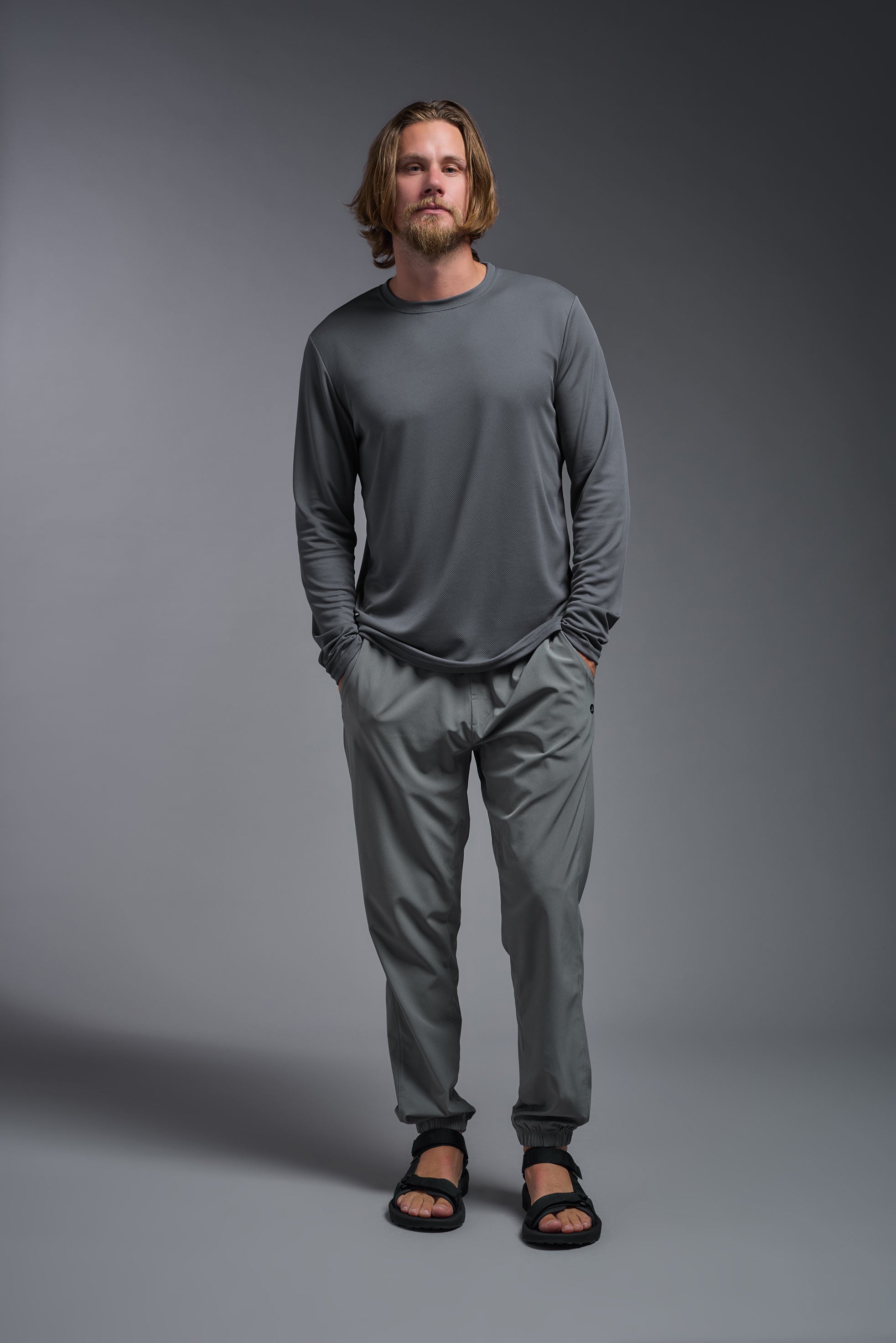 A male model wearing the men's Oxymesh Long Sleeve Tech Tee in the color graphite gray made out of 100% polyester, showing the relaxed fit from a front view. This shirt is breathable, quick-drying, moisture-wicking, and made in the USA. #graphite-gray