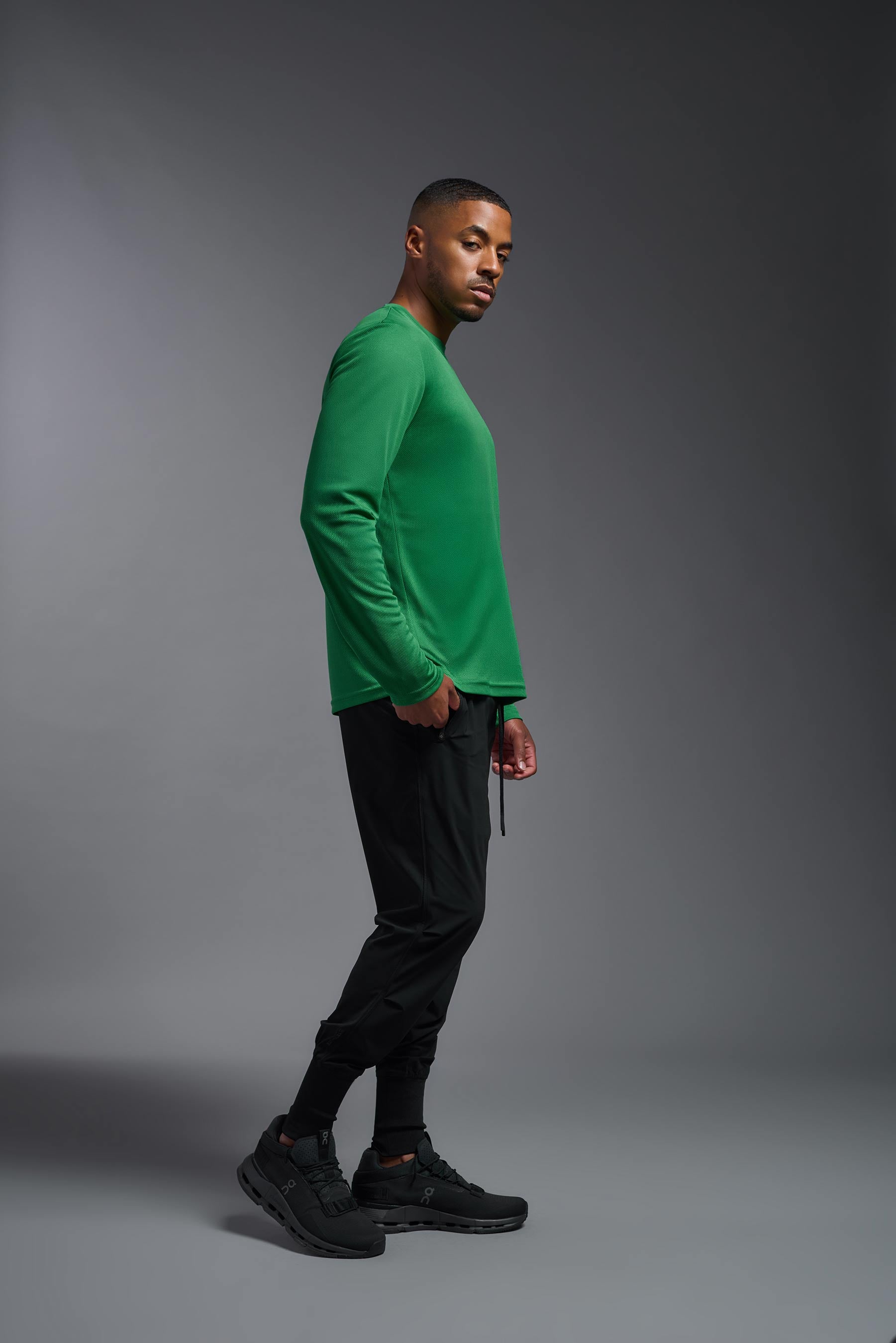 A male model wearing the men's Oxymesh Long Sleeve Tech Tee in the color kelly green, made out of 100% polyester, showing the relaxed fit from a side view. This shirt is breathable, quick-drying, moisture-wicking, and made in the USA. #kelly-green