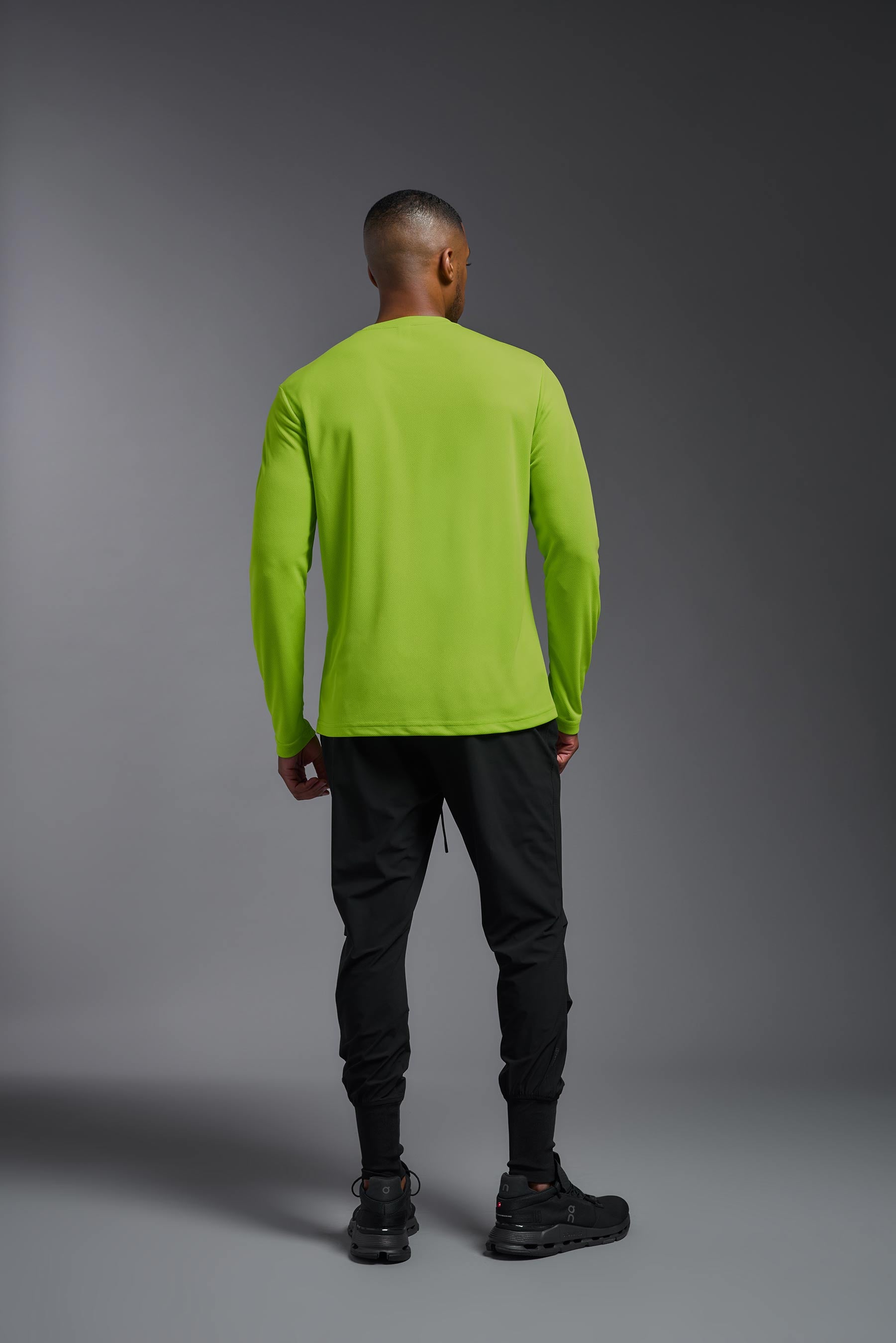 A male model wearing the men's Oxymesh Long Sleeve Tech Tee in the color key lime, made out of 100% polyester, showing the relaxed fit from a back view. This shirt is breathable, quick-drying, moisture-wicking, and made in the USA. #key-lime