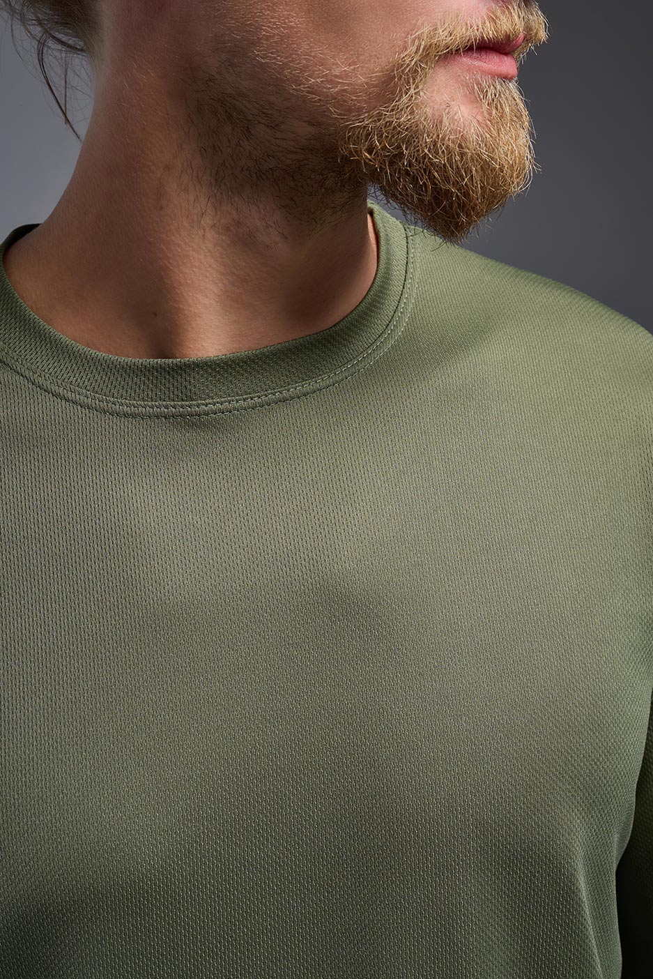 A male model wearing the men's Oxymesh Long Sleeve Tech Tee in the color military green, made out of 100% polyester, showing the relaxed fit from a close-up collar view. This shirt is breathable, quick-drying, moisture-wicking, and made in the USA. #military-green
