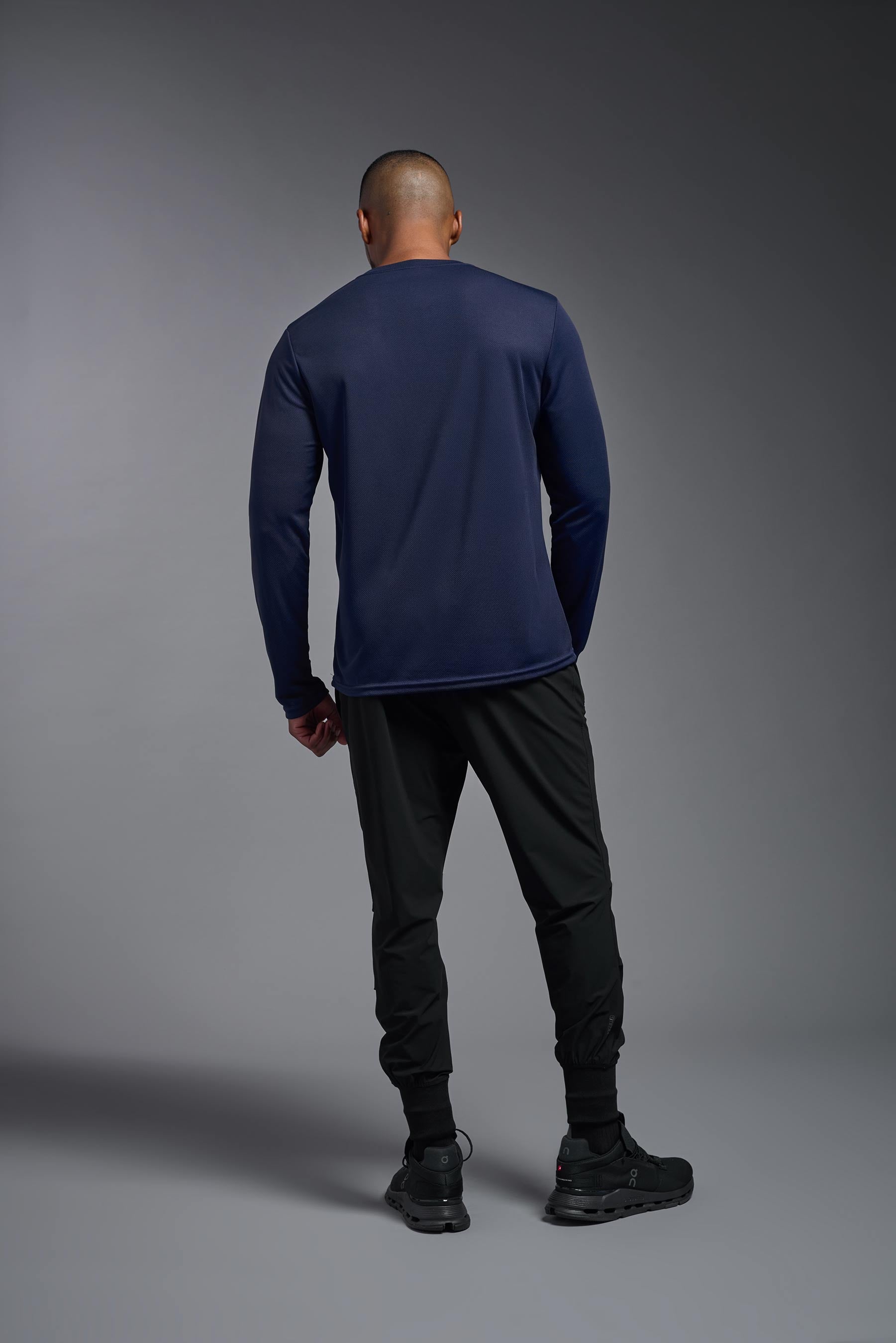A male model wearing the men's Oxymesh Long Sleeve Tech Tee in the color navy blue, made out of 100% polyester, showing the relaxed fit from a back collar view. This shirt is breathable, quick-drying, moisture-wicking, and made in the USA. #navy-blue