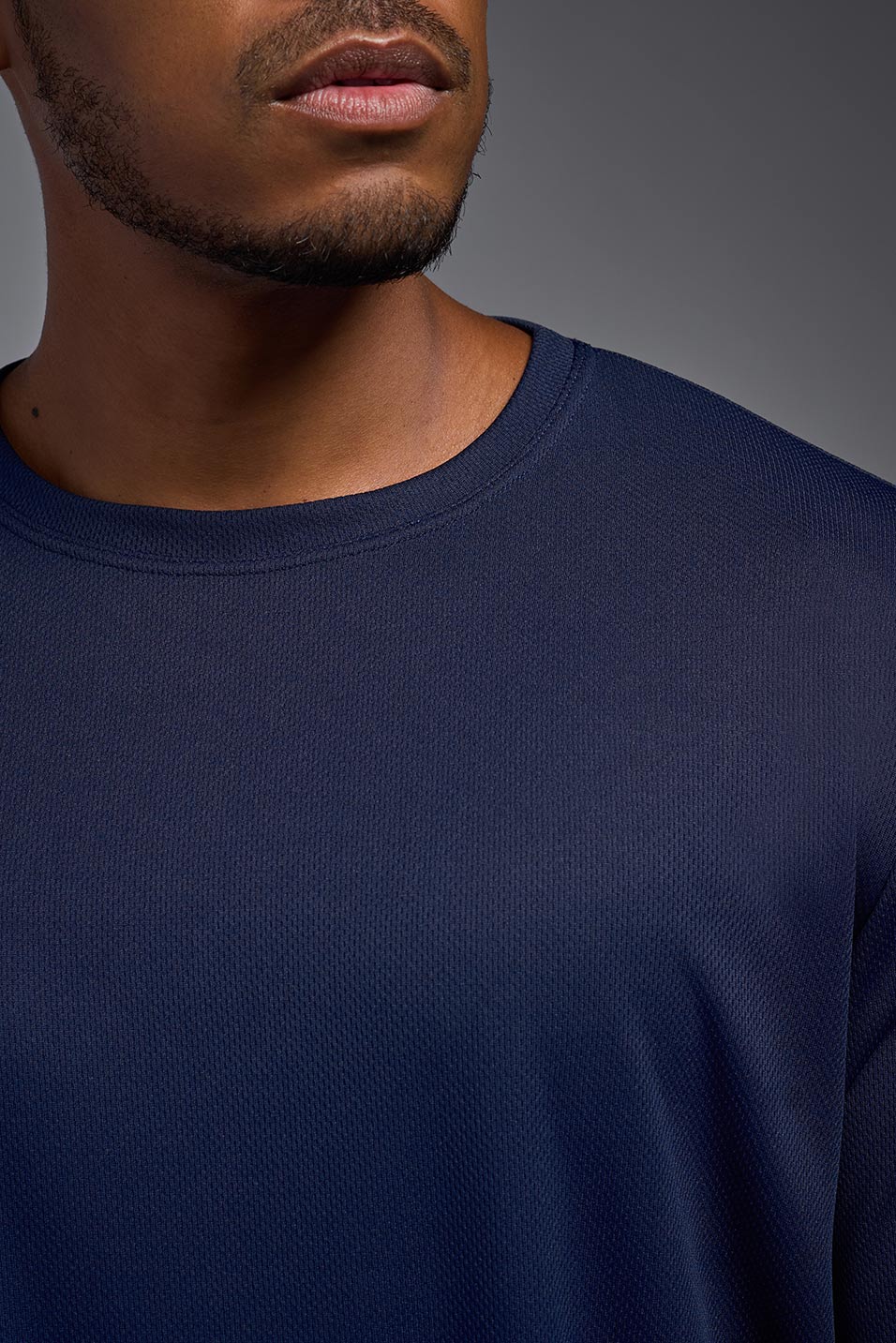A male model wearing the men's Oxymesh Long Sleeve Tech Tee in the color navy blue, made out of 100% polyester, showing the relaxed fit from a close-up collar view. This shirt is breathable, quick-drying, moisture-wicking, and made in the USA. #navy-blue