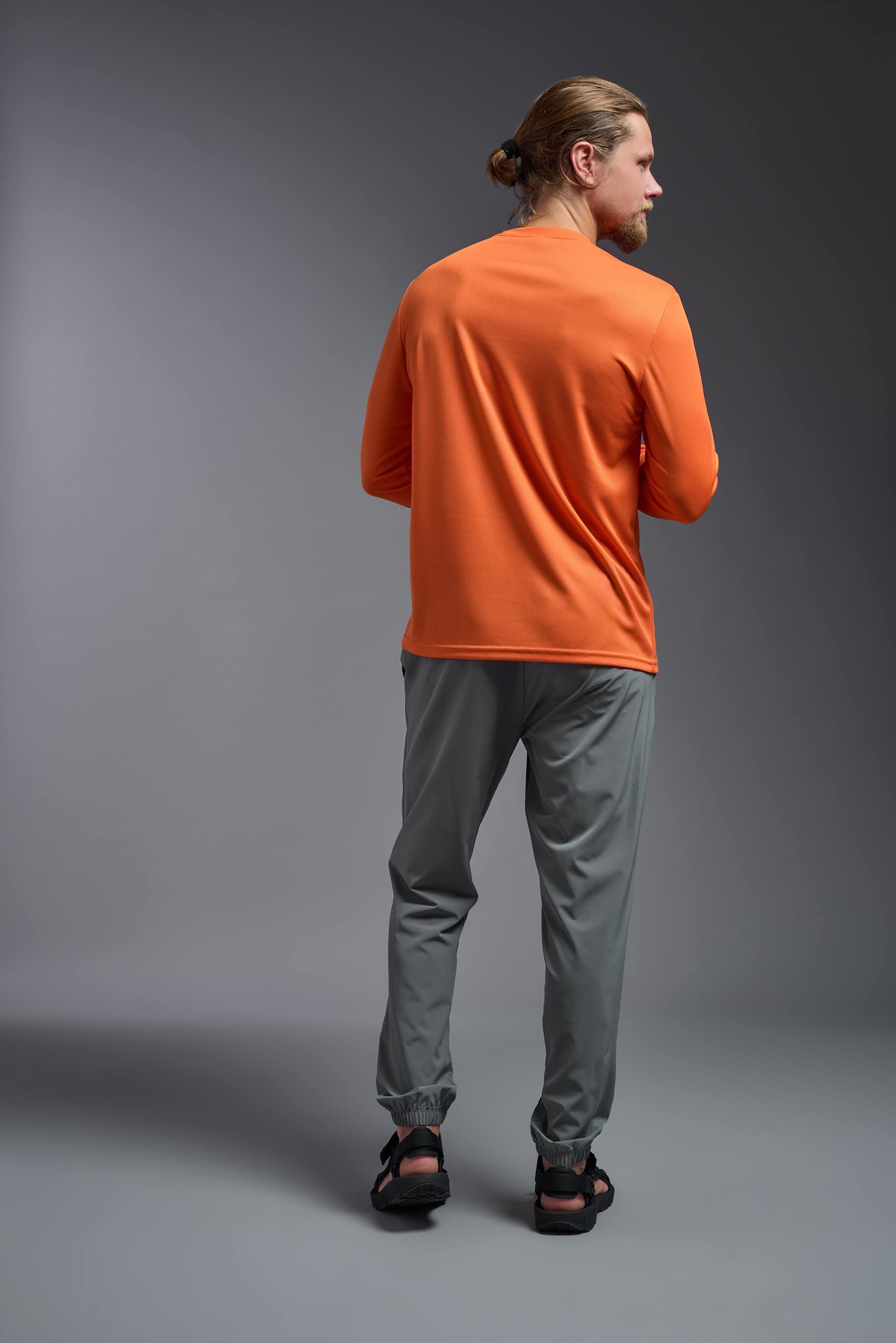 A male model wearing the men's Oxymesh Long Sleeve Tech Tee in the color orange made out of 100% polyester, showing the relaxed fit from a back view. This shirt is breathable, quick-drying, moisture-wicking, and made in the USA. #orange